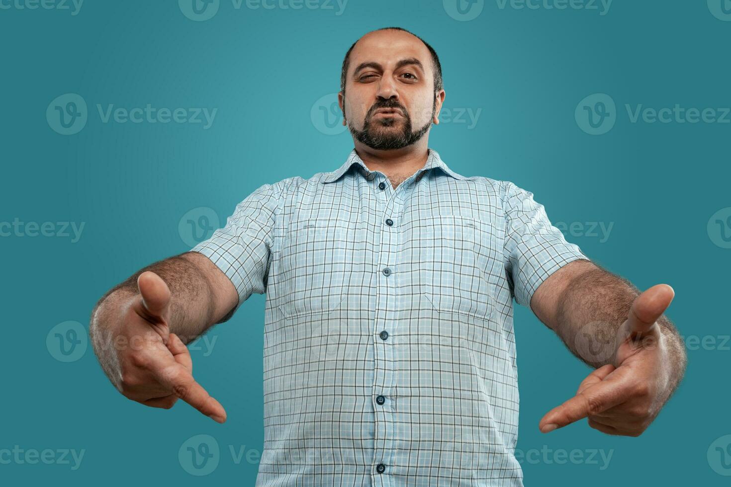 Close-up portrait of a brunet middle-aged man with beard, dressed in a light checkered shirt and posing against a blue background. photo