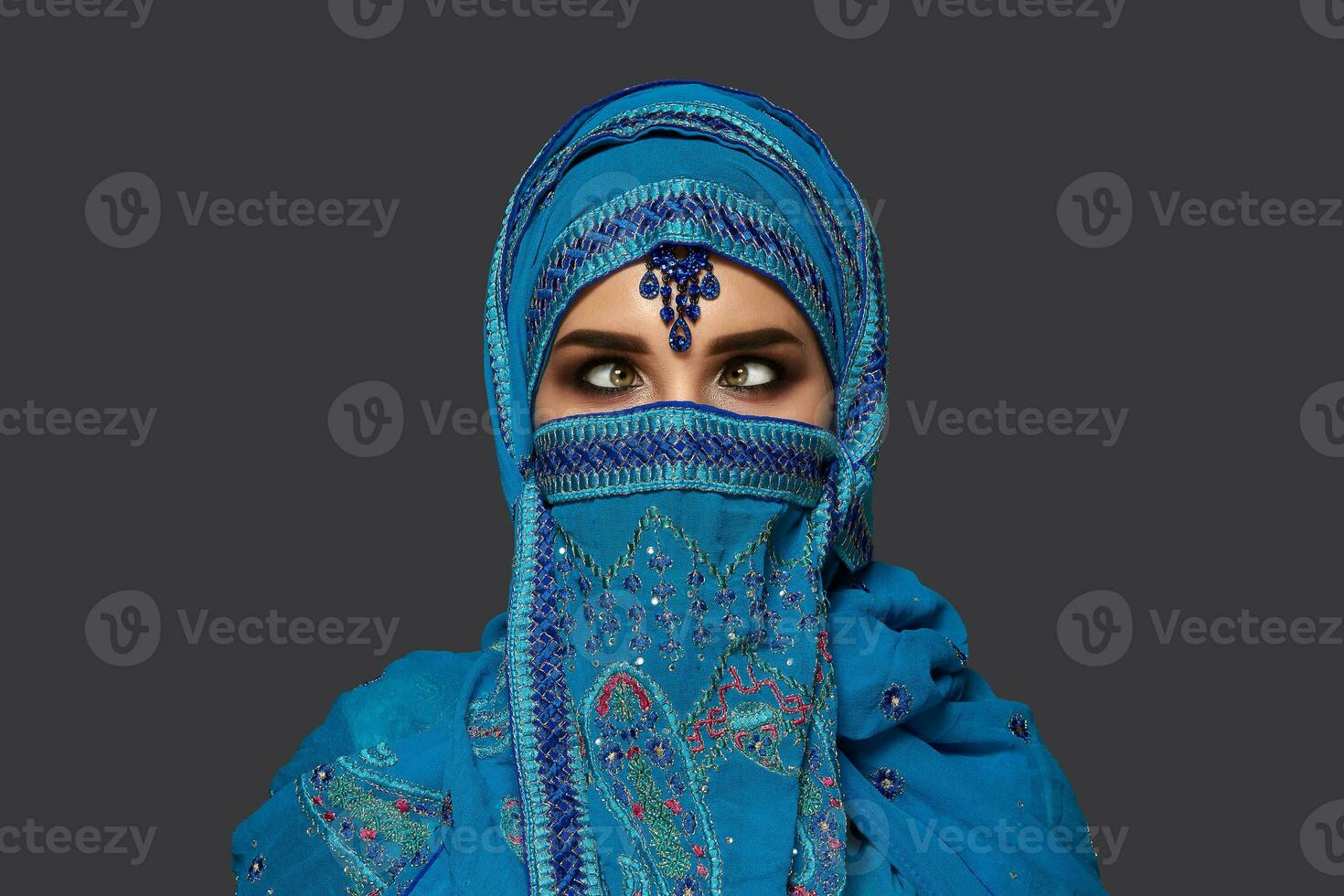 Studio shot of a young beautiful woman wearing the blue hijab decorated with sequins and jewelry. Arabic style. photo