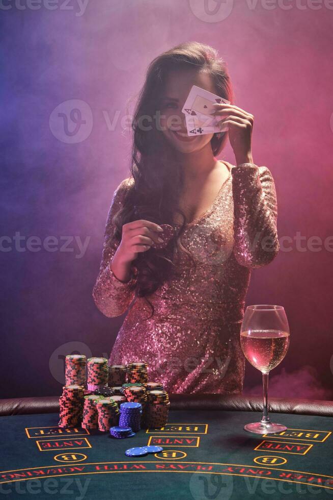 Brunette girl with a perfect hairstyle and bright make-up is posing with playing cards and gambling chips in her hands. Casino, poker. photo