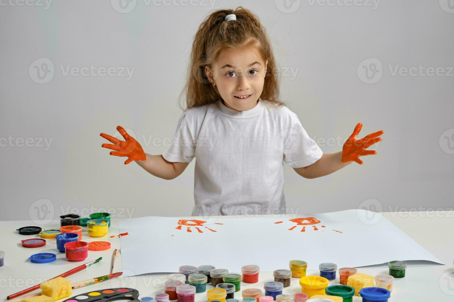 pequeño niña en blanco camiseta sentado a mesa con qué hombre y vistoso pinturas, demostración su pintado manos. aislado en blanco. medio de cerca. foto