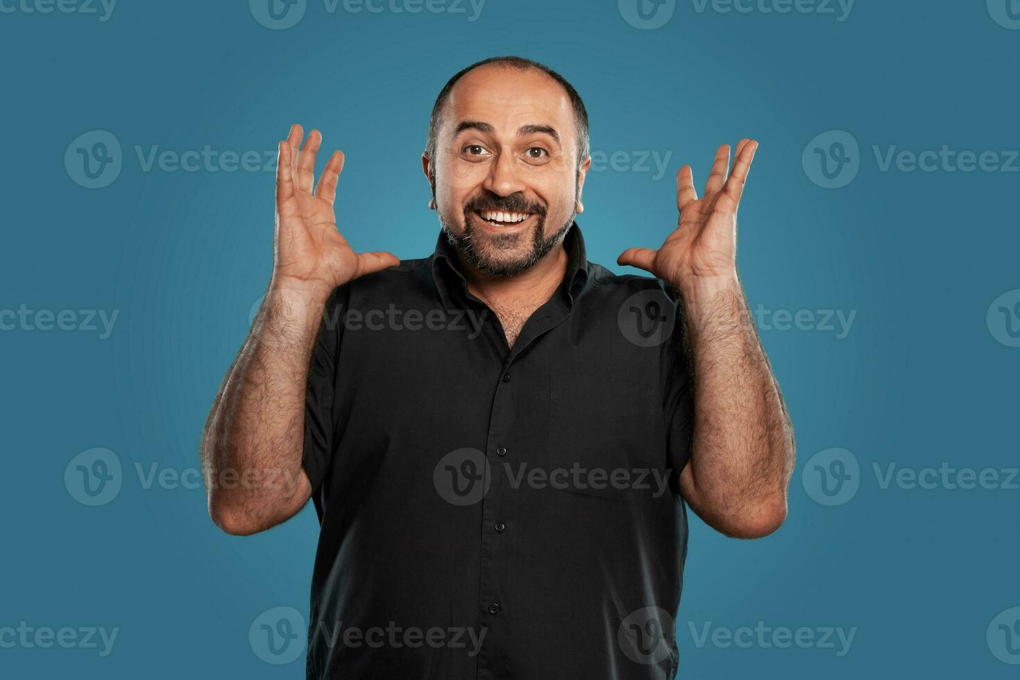 de cerca retrato de un moreno de edad mediana hombre con barba, vestido en un negro camiseta y posando en contra un azul antecedentes. foto