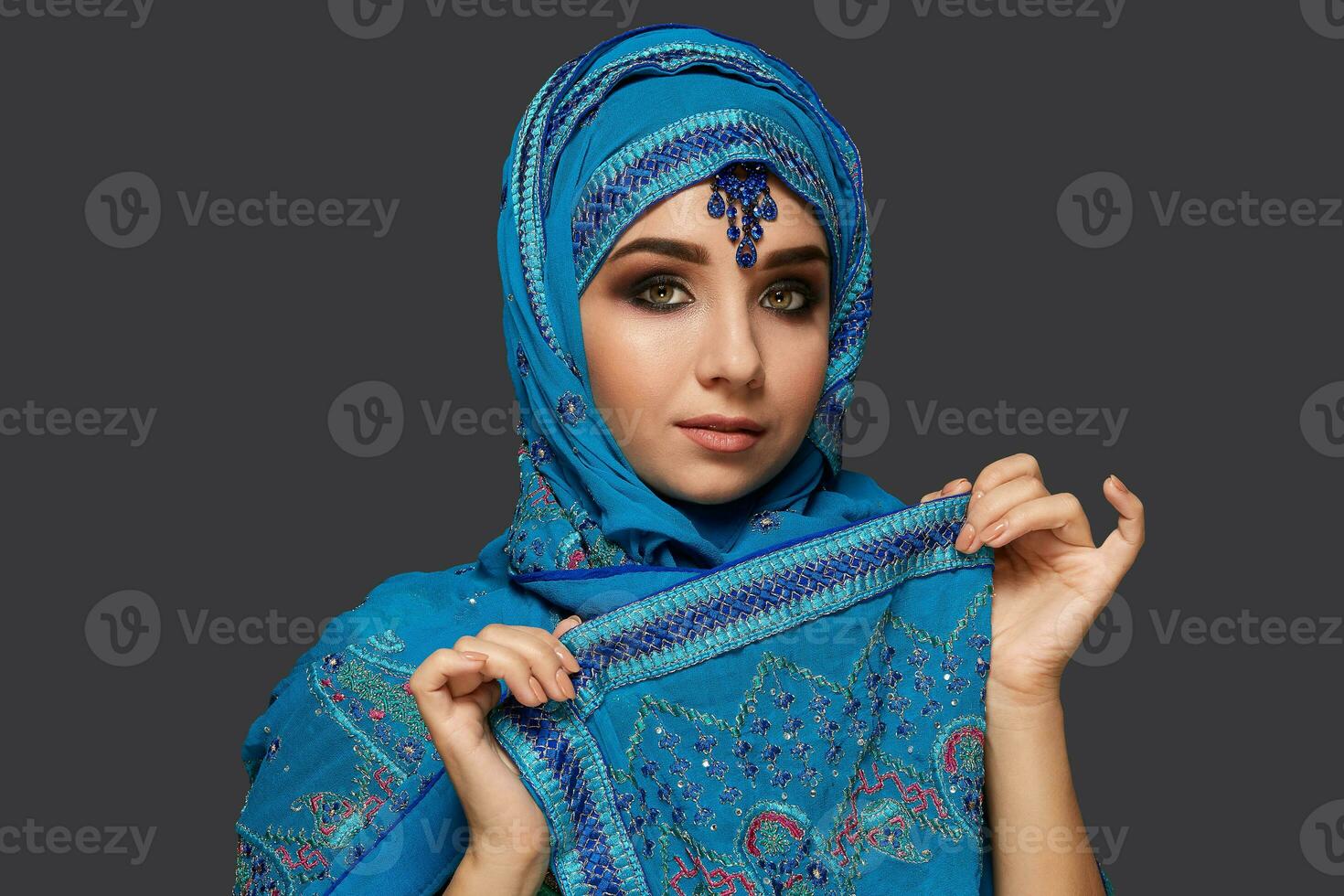 Studio shot of a young beautiful woman wearing the blue hijab decorated with sequins and jewelry. Arabic style. photo
