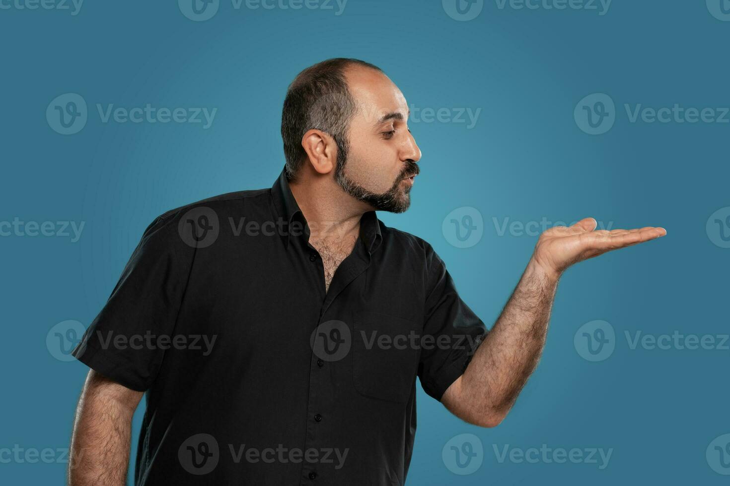 de cerca retrato de un moreno de edad mediana hombre con barba, vestido en un negro camiseta y posando en contra un azul antecedentes. foto