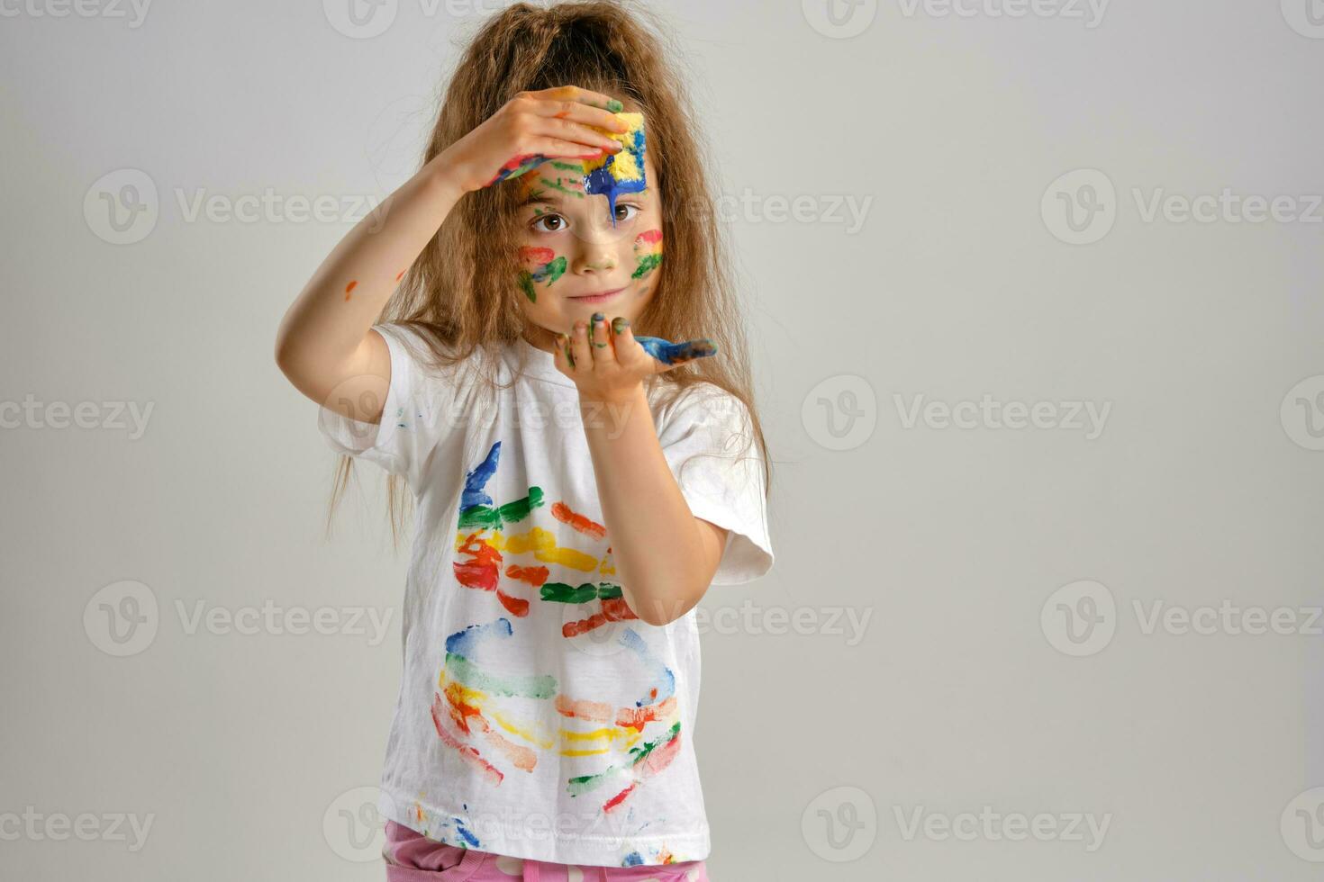 pequeño niña en blanco pintado camiseta, con de colores cara es jugando con un esponja mojado en pintar. aislado en blanco. de cerca. foto