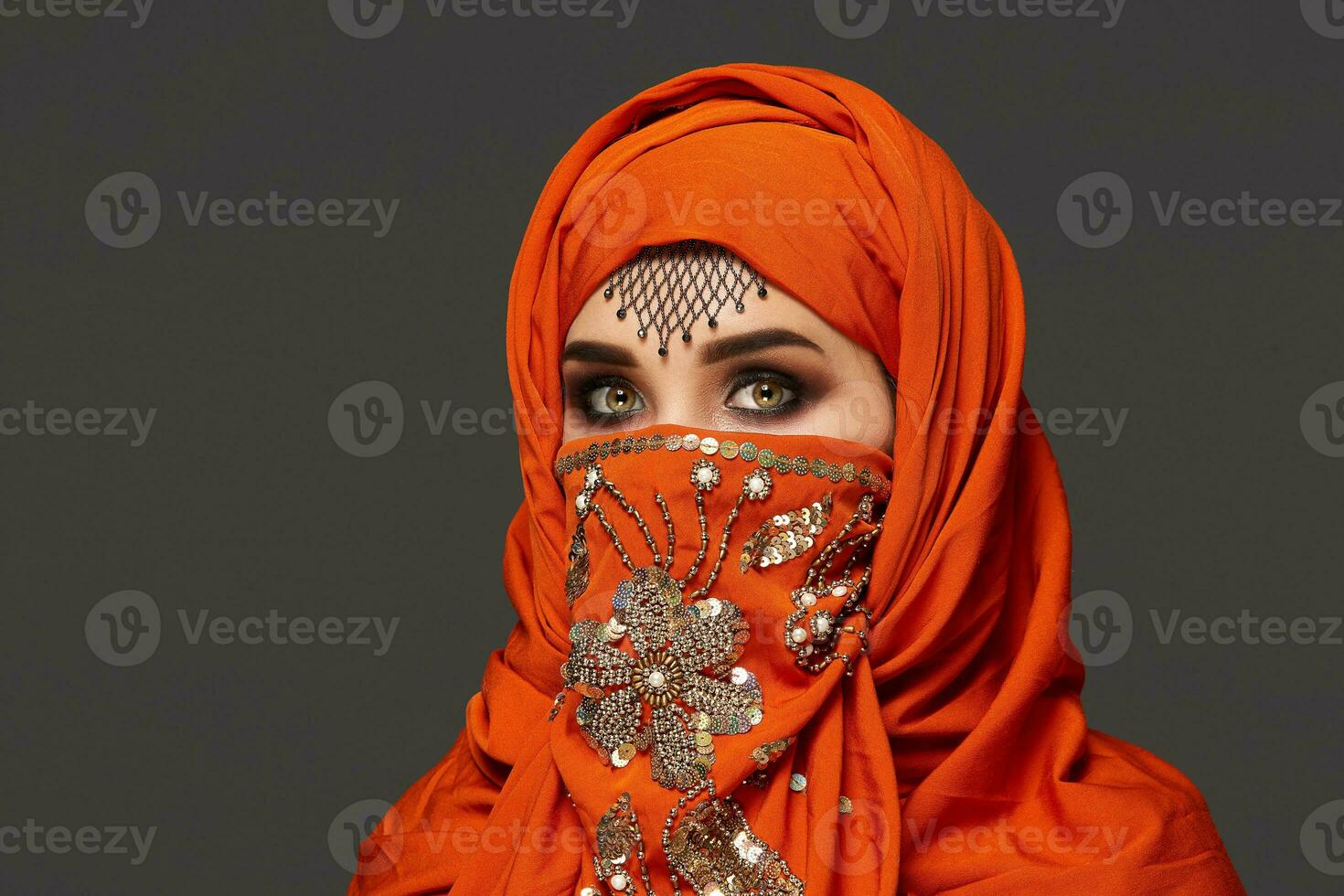 Studio shot of a young charming woman wearing the terracotta hijab decorated with sequins and jewelry. Arabic style. photo