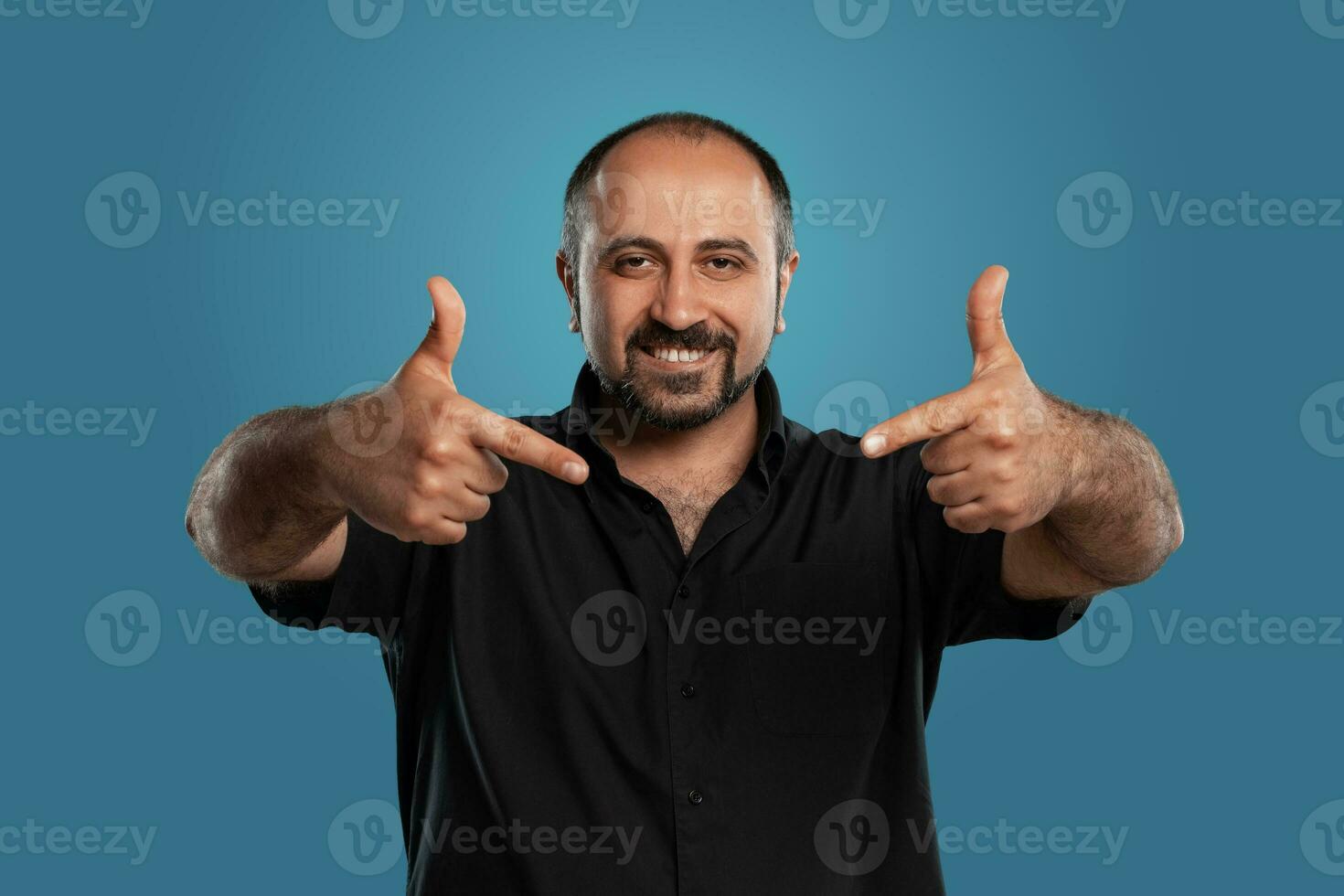 de cerca retrato de un moreno de edad mediana hombre con barba, vestido en un negro camiseta y posando en contra un azul antecedentes. foto