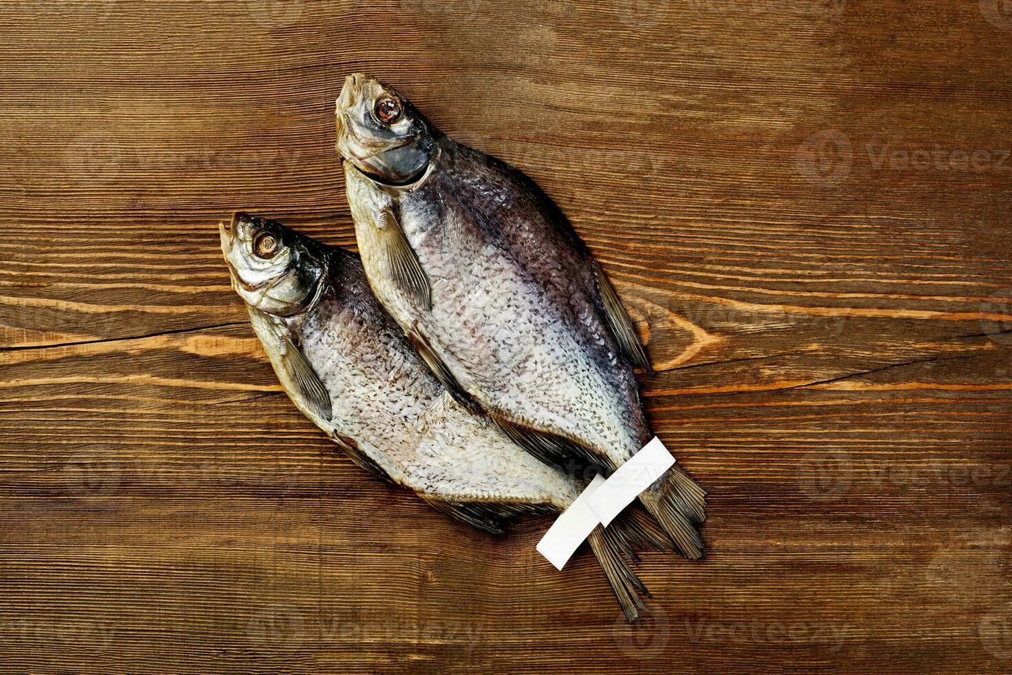Two salted jerked roach fish with labels on tails on wooden background photo