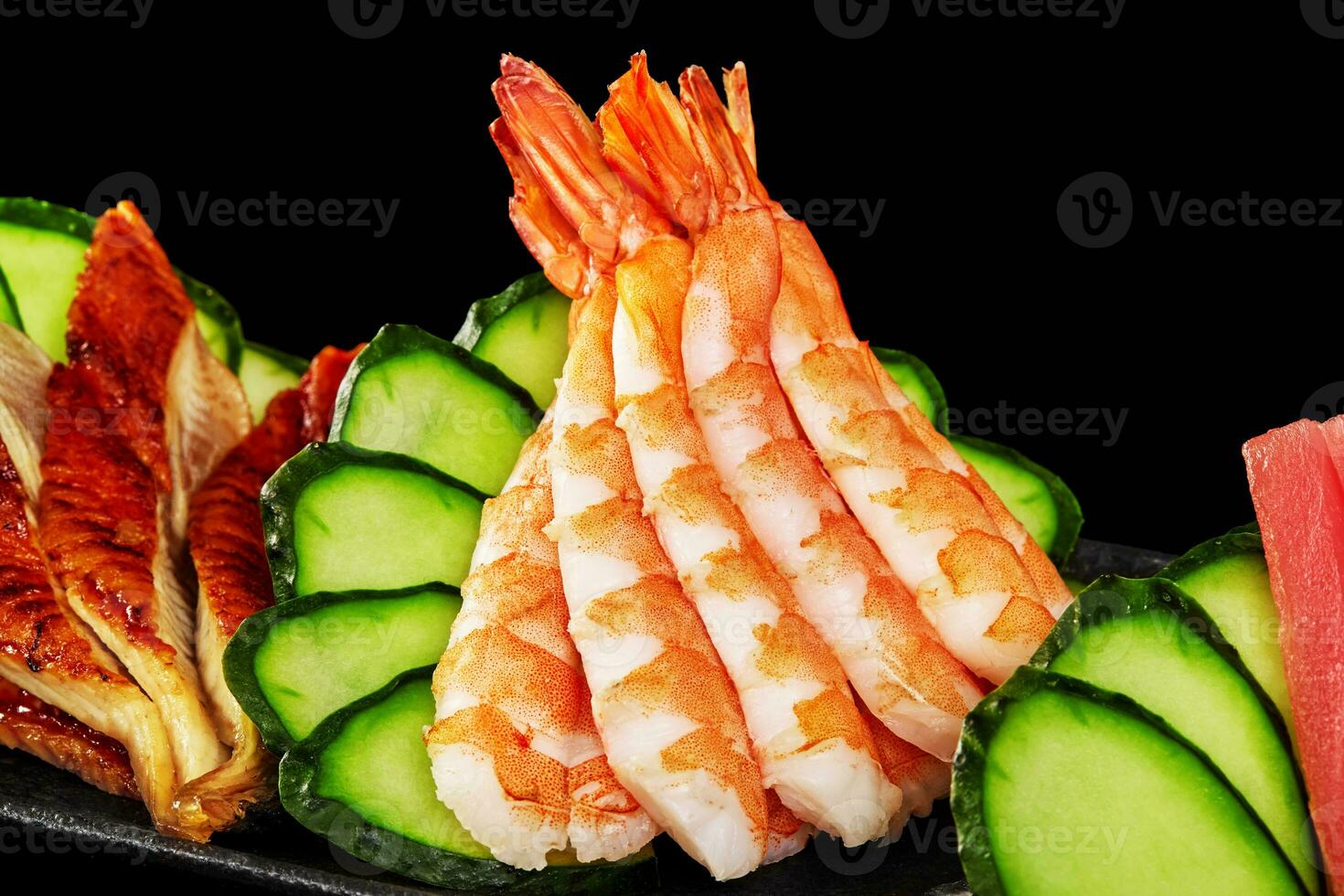 Closeup of lightly poached shrimps on platter with grilled unagi eel, tuna sashimi and cucumber photo