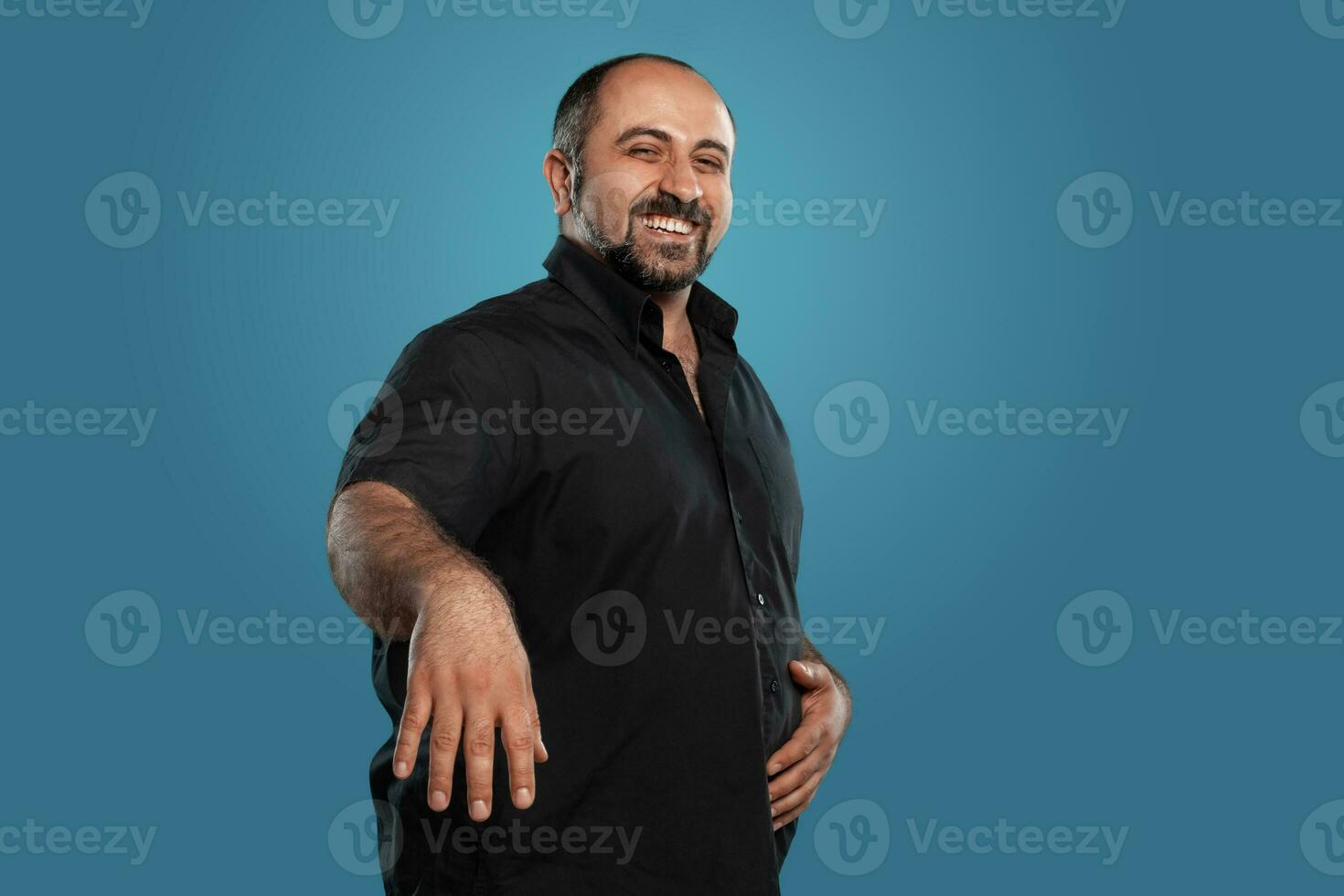 Close-up portrait of a brunet middle-aged man with beard, dressed in a black t-shirt and posing against a blue background. photo