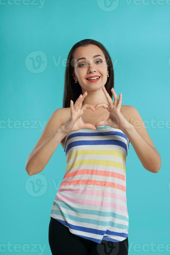 Brunette woman with long hair, dressed in striped shirt and black leggings, posing against blue studio background. Sincere emotions. Close-up. photo