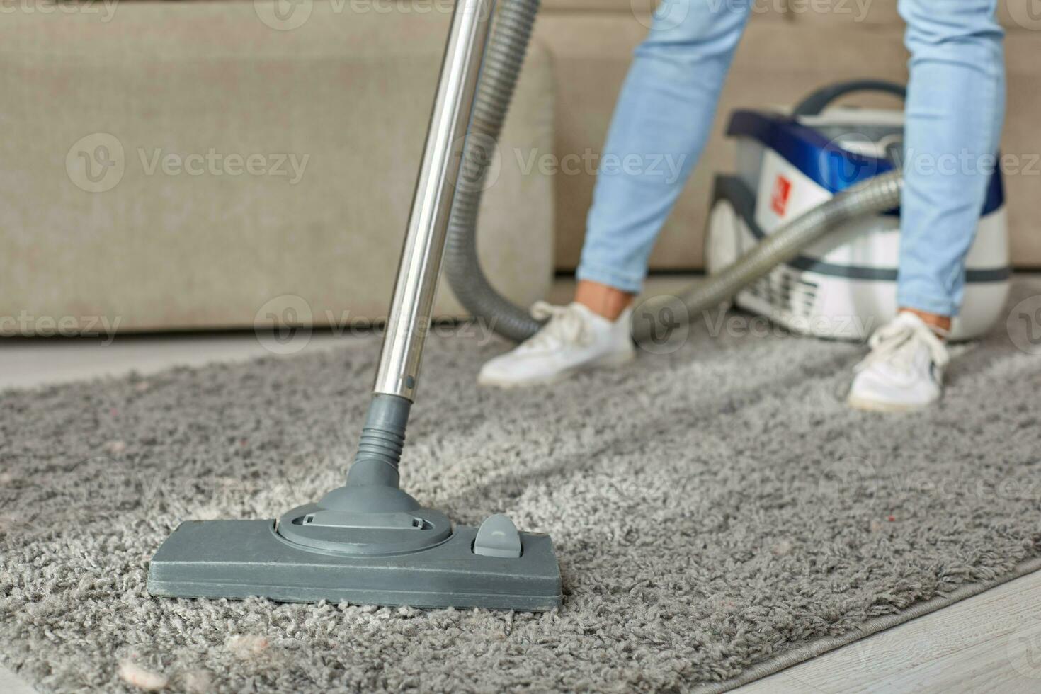 Cropped image of beautiful young woman using a vacuum cleaner while cleaning carpet in the house photo