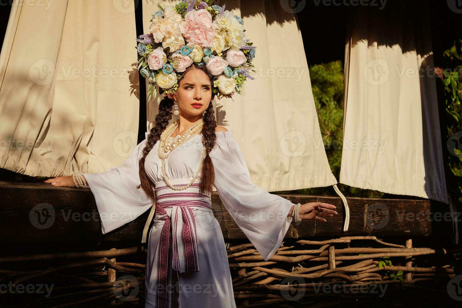 Brunette girl in a white ukrainian authentic national costume and a wreath of flowers is posing against a terrace. photo