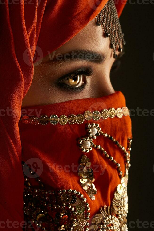 Studio shot of a young charming woman wearing the terracotta hijab decorated with sequins and jewelry. Arabic style. photo