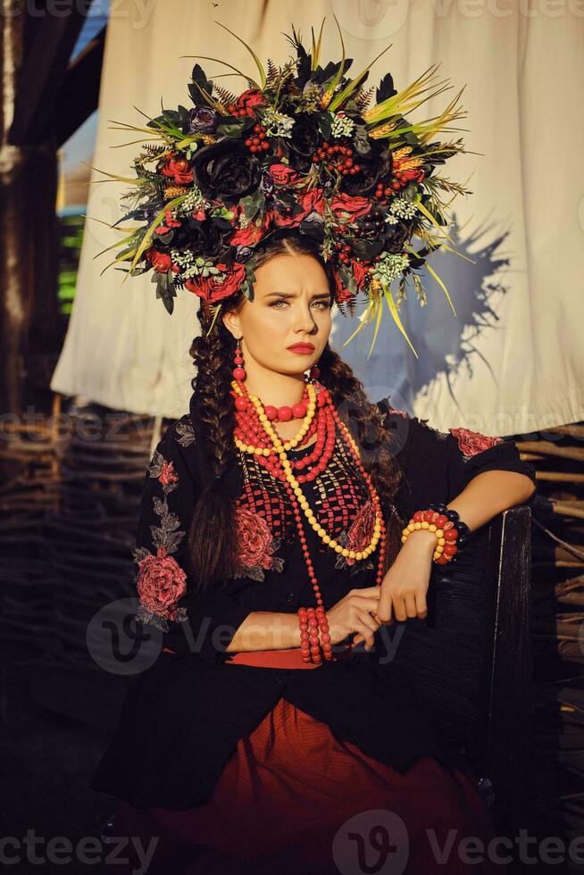 Brunette girl in a black and red embroidered ukrainian authentic national costume and a wreath of flowers is posing against a terrace. Close-up. photo