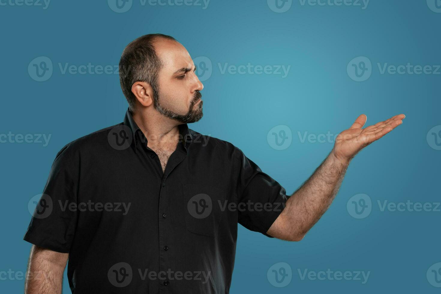 de cerca retrato de un moreno de edad mediana hombre con barba, vestido en un negro camiseta y posando en contra un azul antecedentes. foto