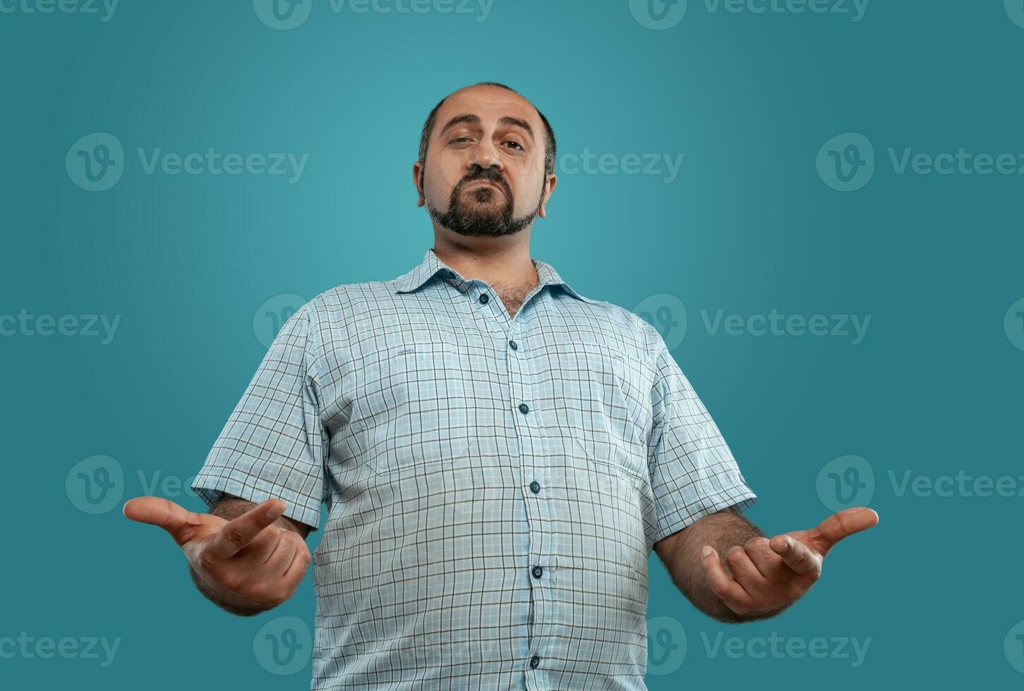 Close-up portrait of a brunet middle-aged man with beard, dressed in a light checkered shirt and posing against a blue background. photo