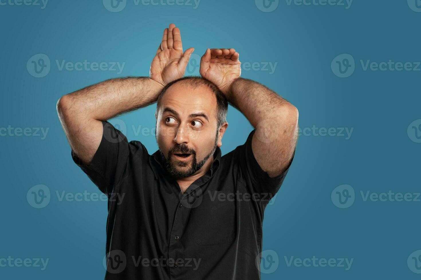 Close-up portrait of a brunet middle-aged man with beard, dressed in a black t-shirt and posing against a blue background. photo
