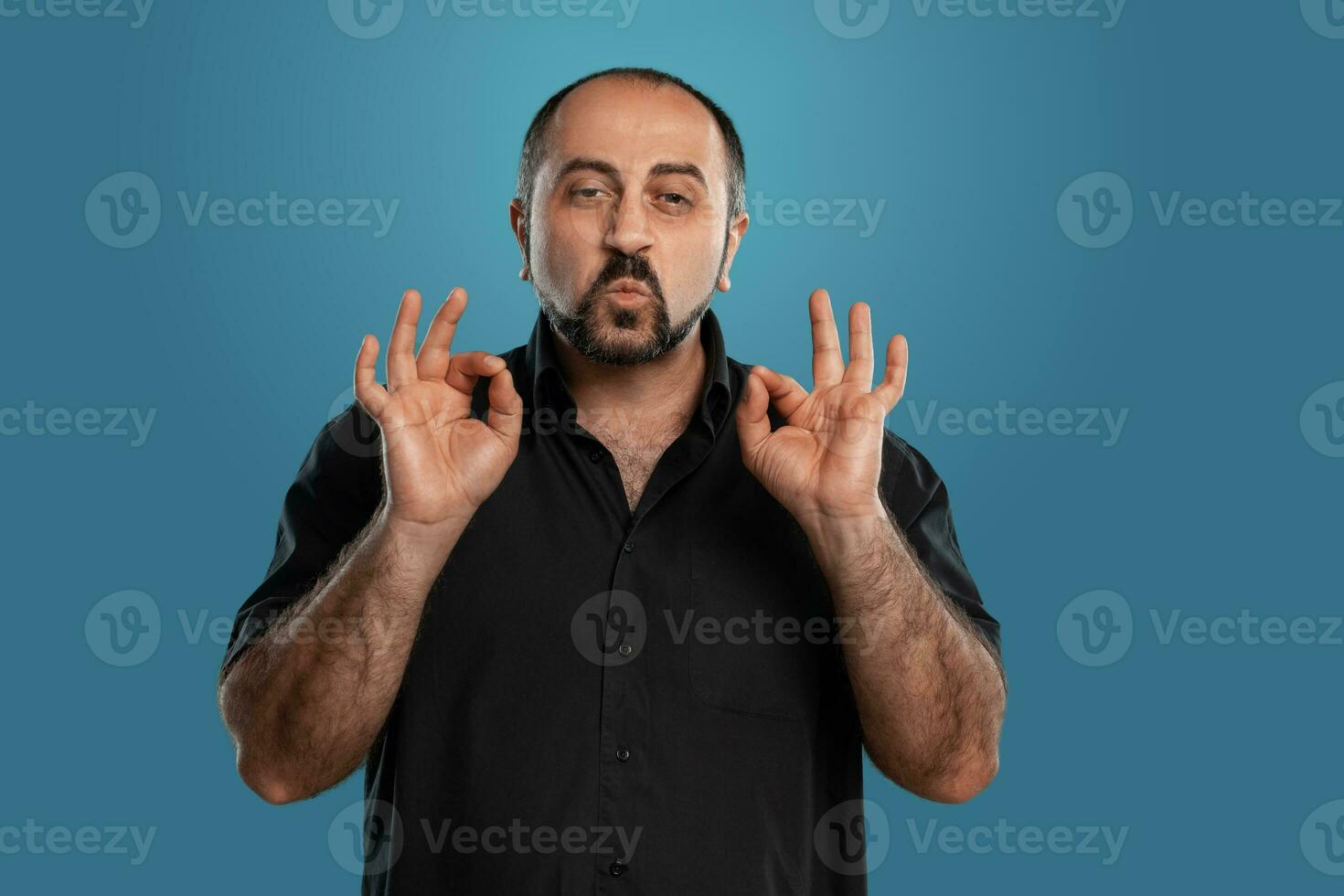 Close-up portrait of a brunet middle-aged man with beard, dressed in a black t-shirt and posing against a blue background. photo