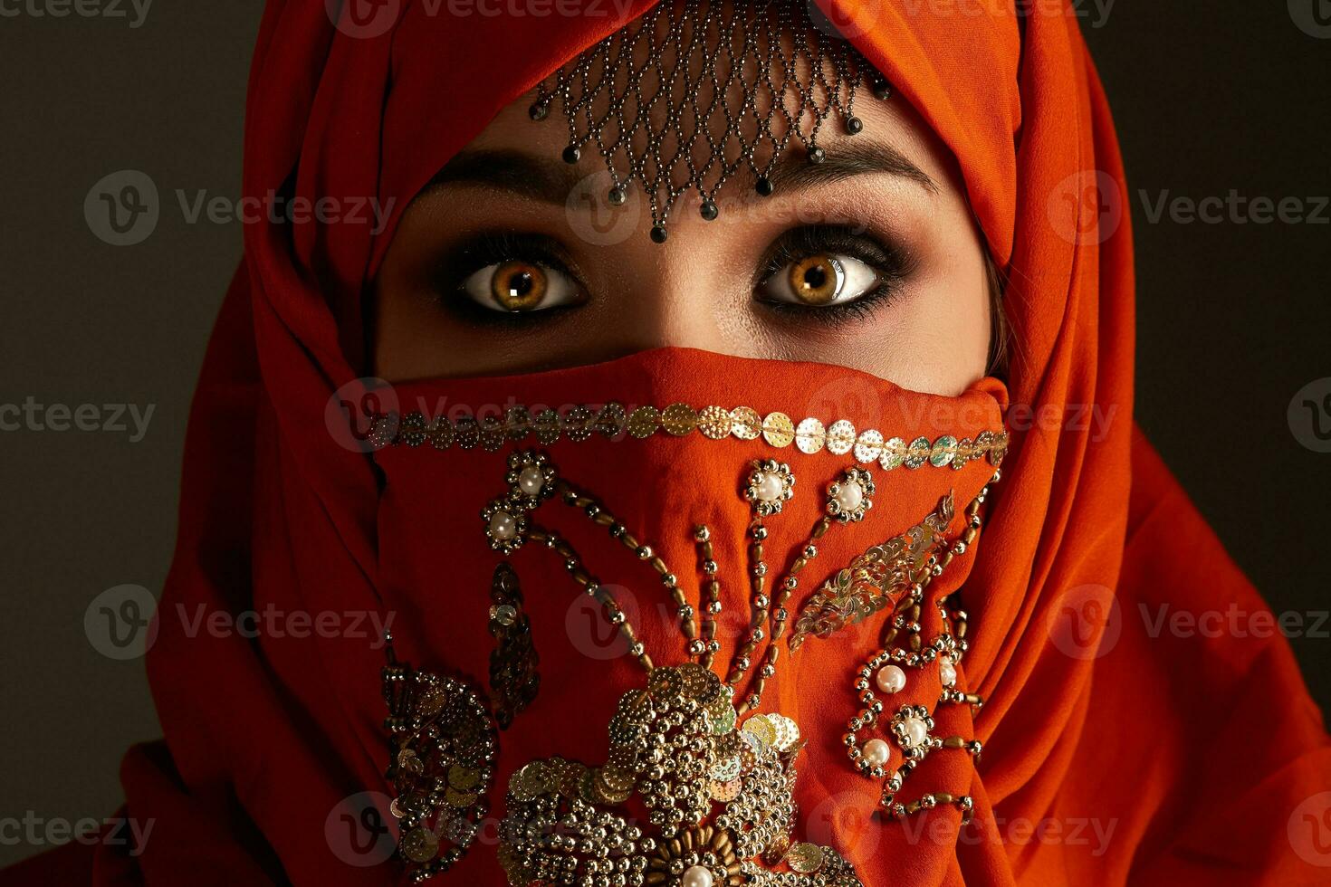 Studio shot of a young charming woman wearing the terracotta hijab decorated with sequins and jewelry. Arabic style. photo