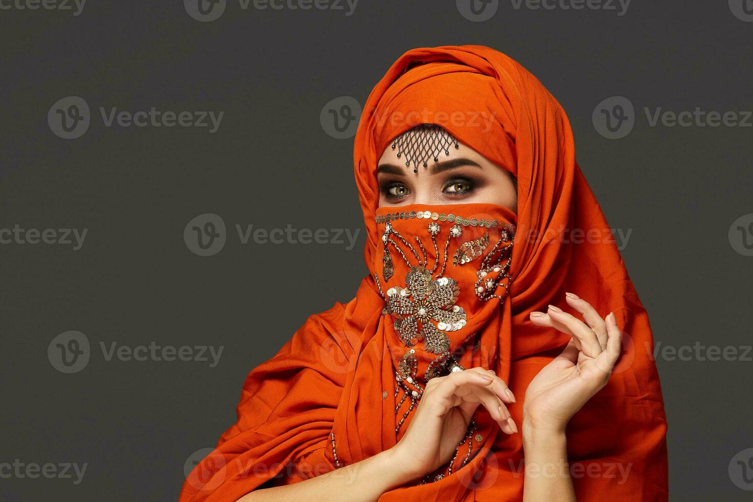 Studio shot of a young charming woman wearing the terracotta hijab decorated with sequins and jewelry. Arabic style. photo