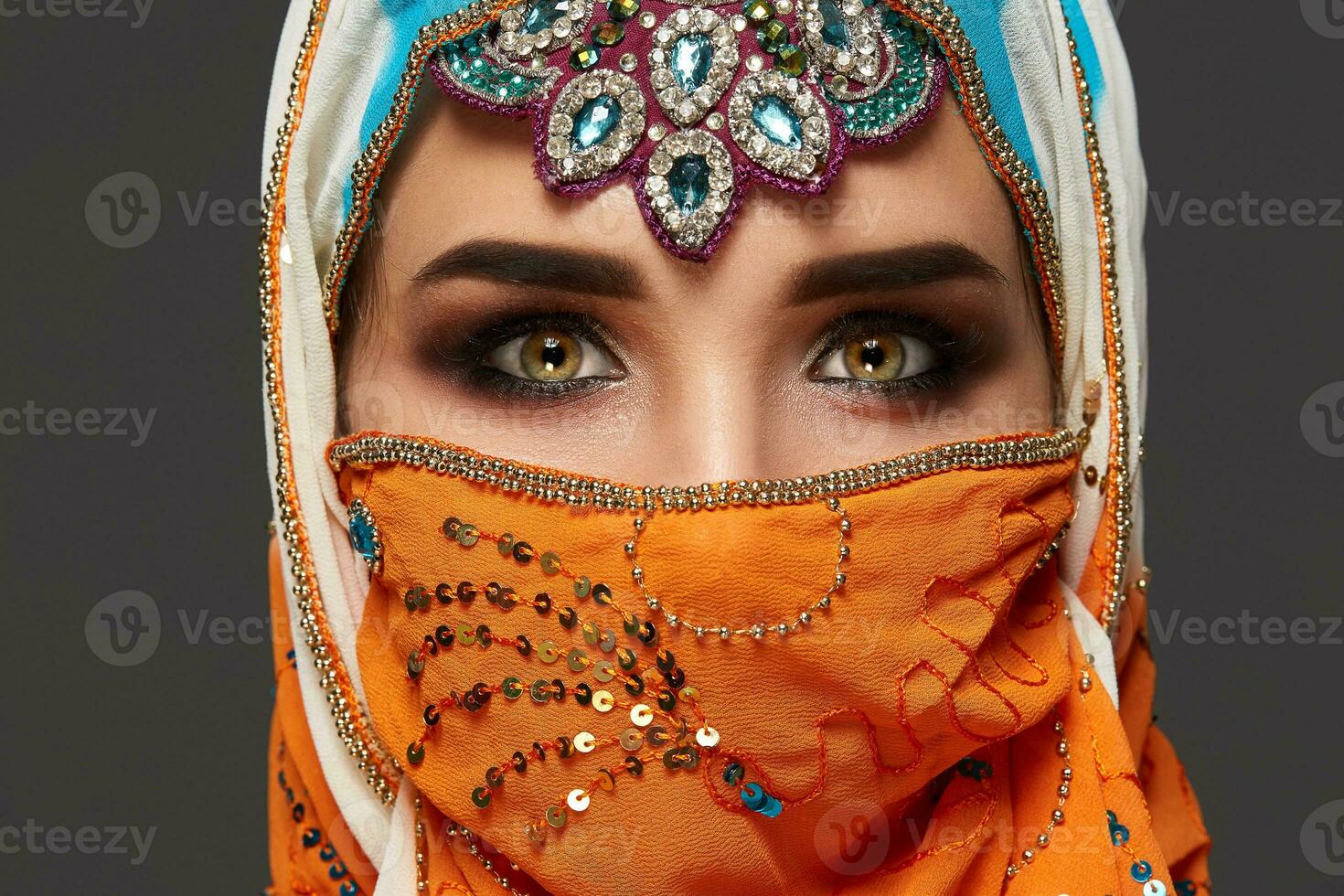 Studio shot of a chrming female wearing the colorful hijab decorated with sequins and jewelry. Arabic style. photo