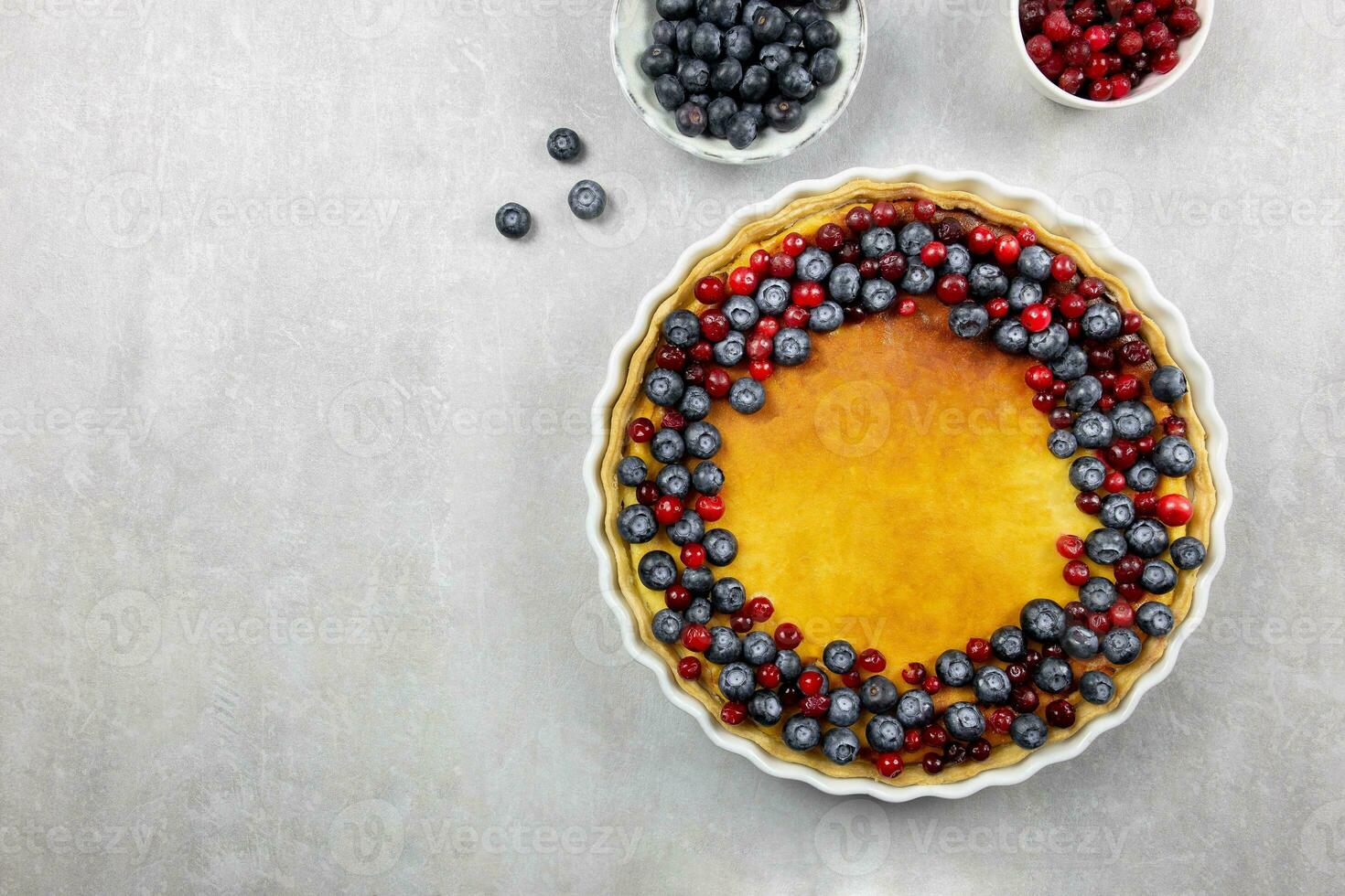 Delicious cheesecake tart with fresh blueberries and cranberries on a light gray concrete background. Top view. Copy space. photo