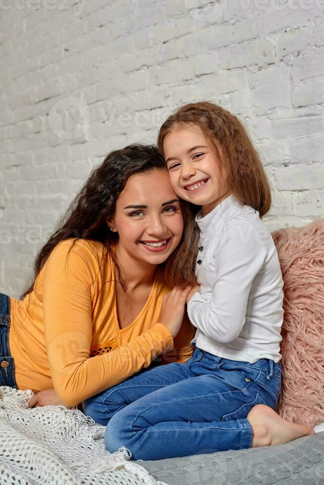 Love of young mother and daughter. They sit on the bed at home and have fun photo