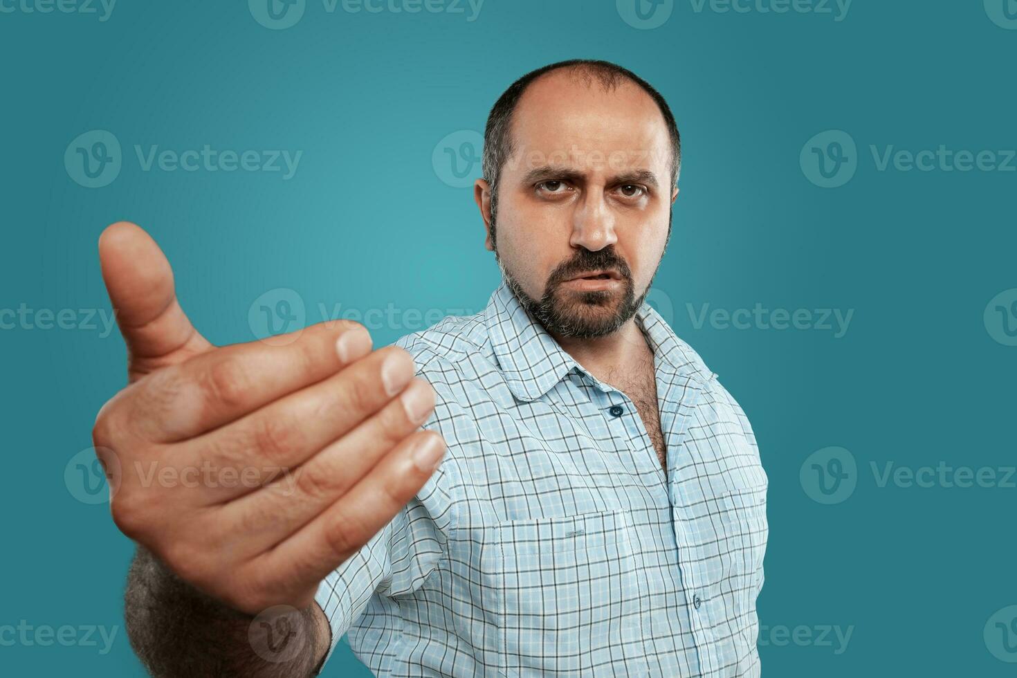 Close-up portrait of a brunet middle-aged man with beard, dressed in a light checkered shirt and posing against a blue background. photo