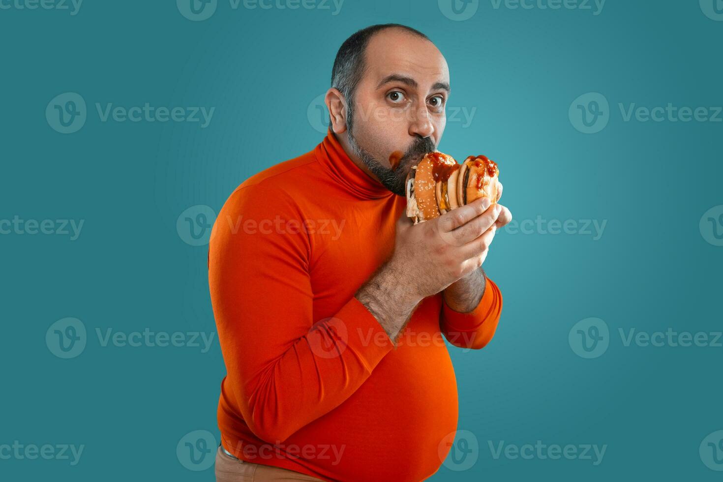 de cerca retrato de un de edad mediana hombre con barba, vestido en un rojo suéter tipo con cuello de tortuga, posando con hamburguesas en contra un azul antecedentes. rápido alimento. foto