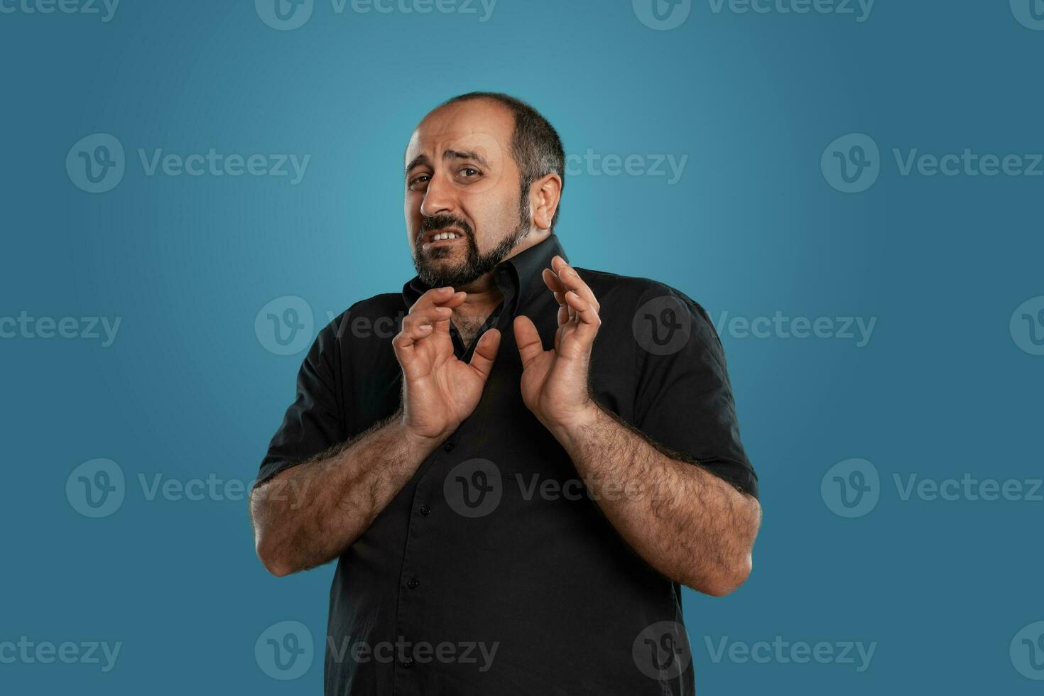Close-up portrait of a brunet middle-aged man with beard, dressed in a black t-shirt and posing against a blue background. photo