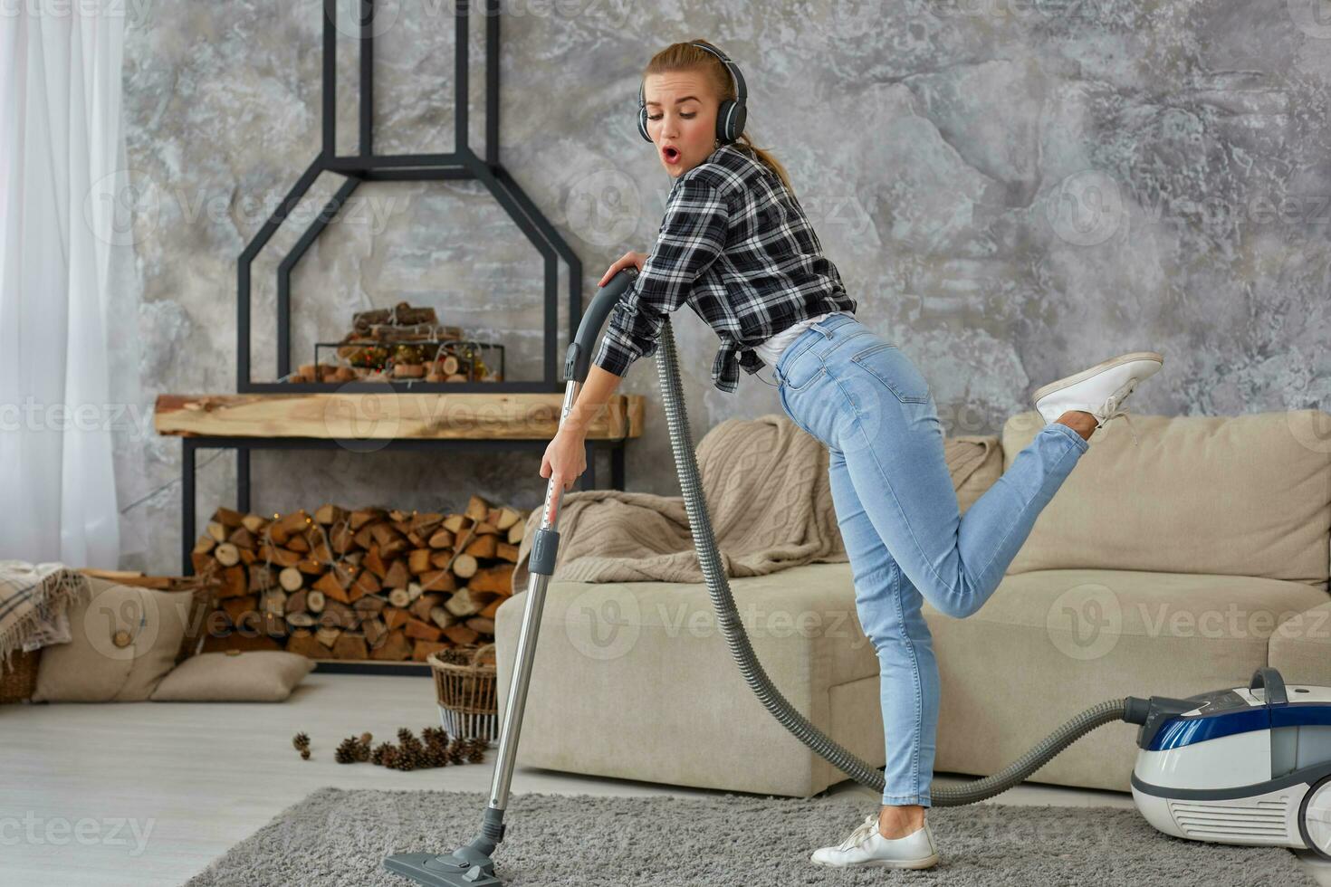 Full length portrait of cheerful young woman 20s listening to music via headphones and having fun with vacuum cleaner in the house. photo