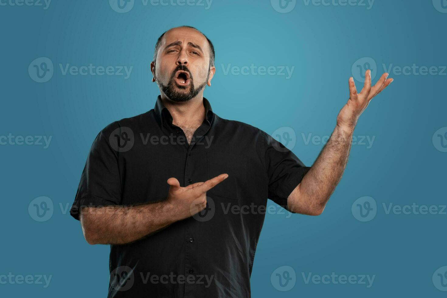 Close-up portrait of a brunet middle-aged man with beard, dressed in a black t-shirt and posing against a blue background. photo