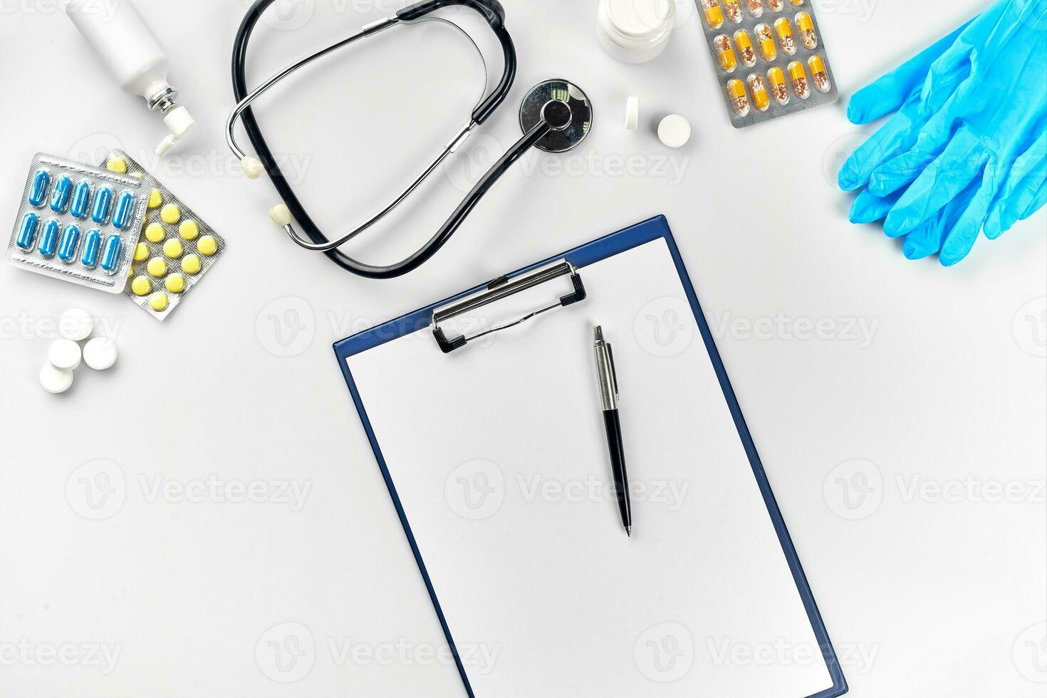 Medical equipment pills, blue gloves, thermometer and stethoscope, white blank with a pen on white background. Top view. Copy space photo