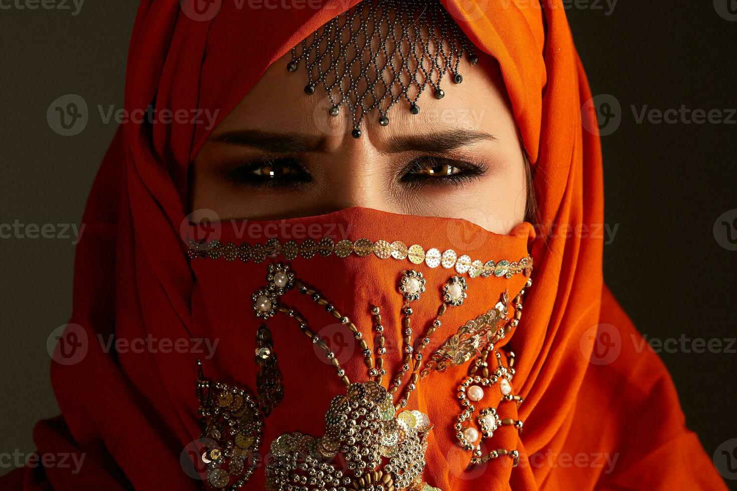 Studio shot of a young charming woman wearing the terracotta hijab decorated with sequins and jewelry. Arabic style. photo