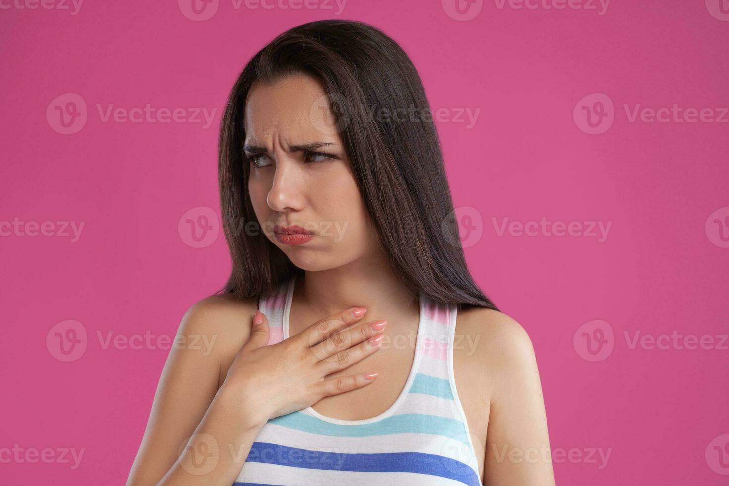 Brunette woman with long hair, dressed in colorful striped shirt, posing against pink studio background. Sincere emotions. Close-up. photo