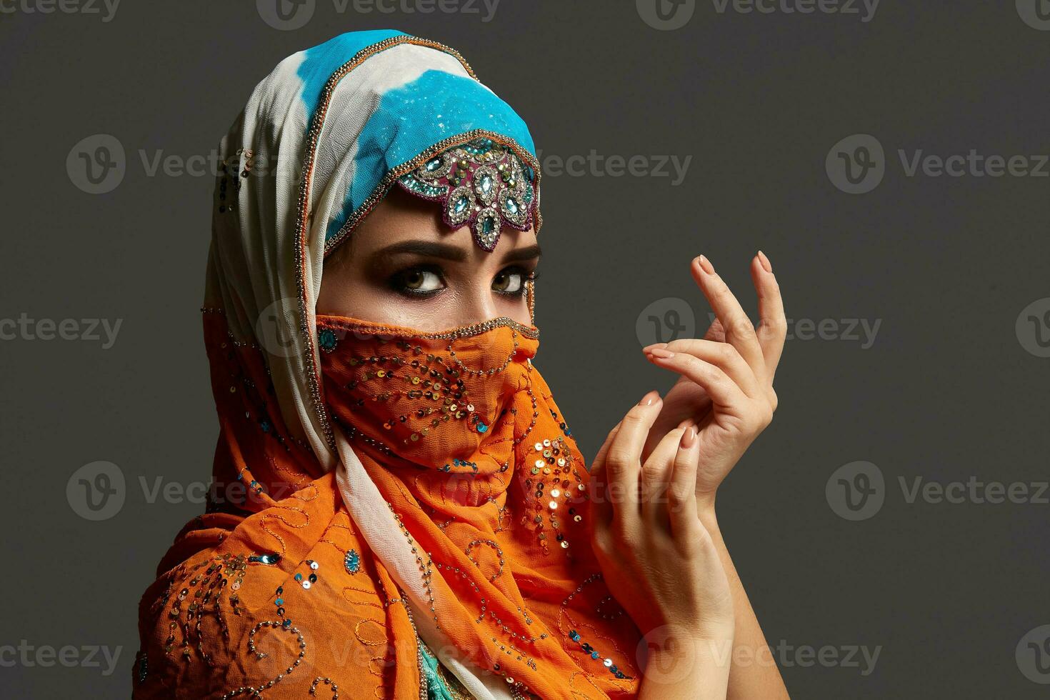 Studio shot of a chrming female wearing the colorful hijab decorated with sequins and jewelry. Arabic style. photo