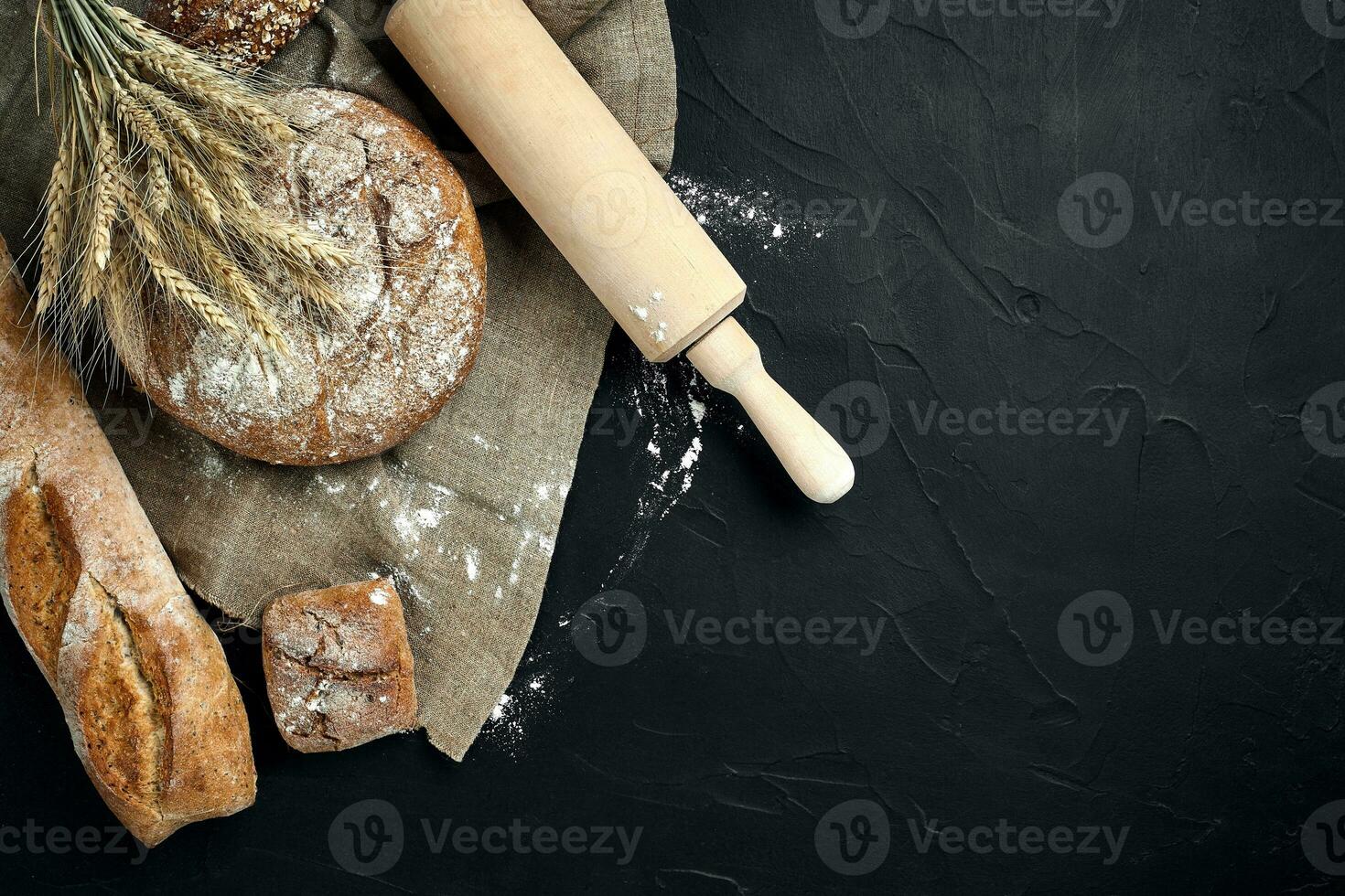 Top view of baguette, baked bread, flour and wheat spikes composition with wheat flour sprinkled around on a dark background photo