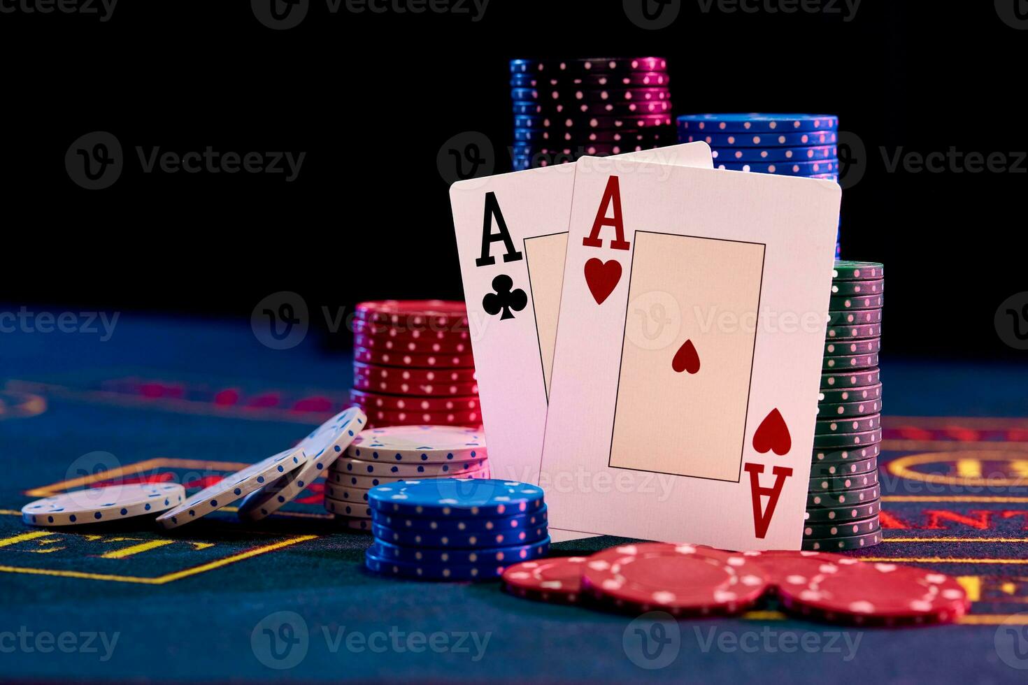 Two aces standing leaning on chips piles, some of them are laying nearby on blue cover of playing table. Black background. Casino concept. Close-up. photo