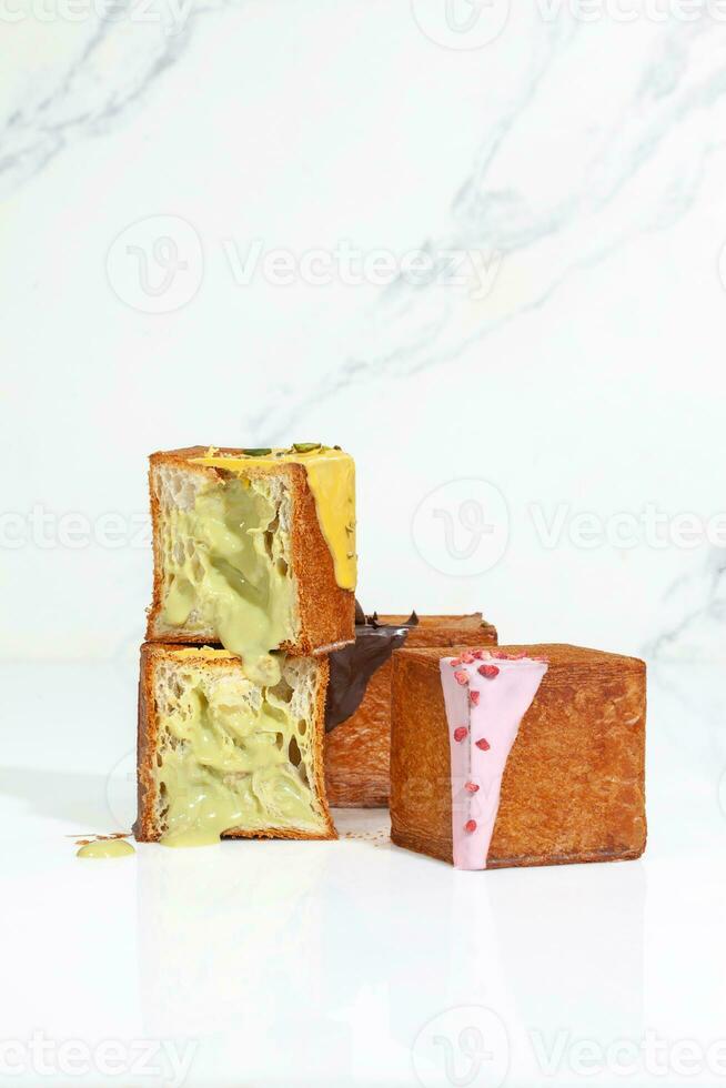 Sliced cube shaped croissant with pistachio cream and two whole with berry glaze and chocolate ganache photo