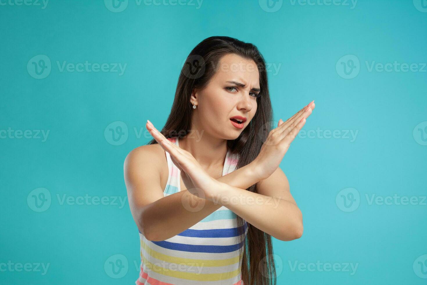 Brunette woman with long hair, dressed in colorful striped shirt, posing against blue studio background. Sincere emotions. Close-up. photo