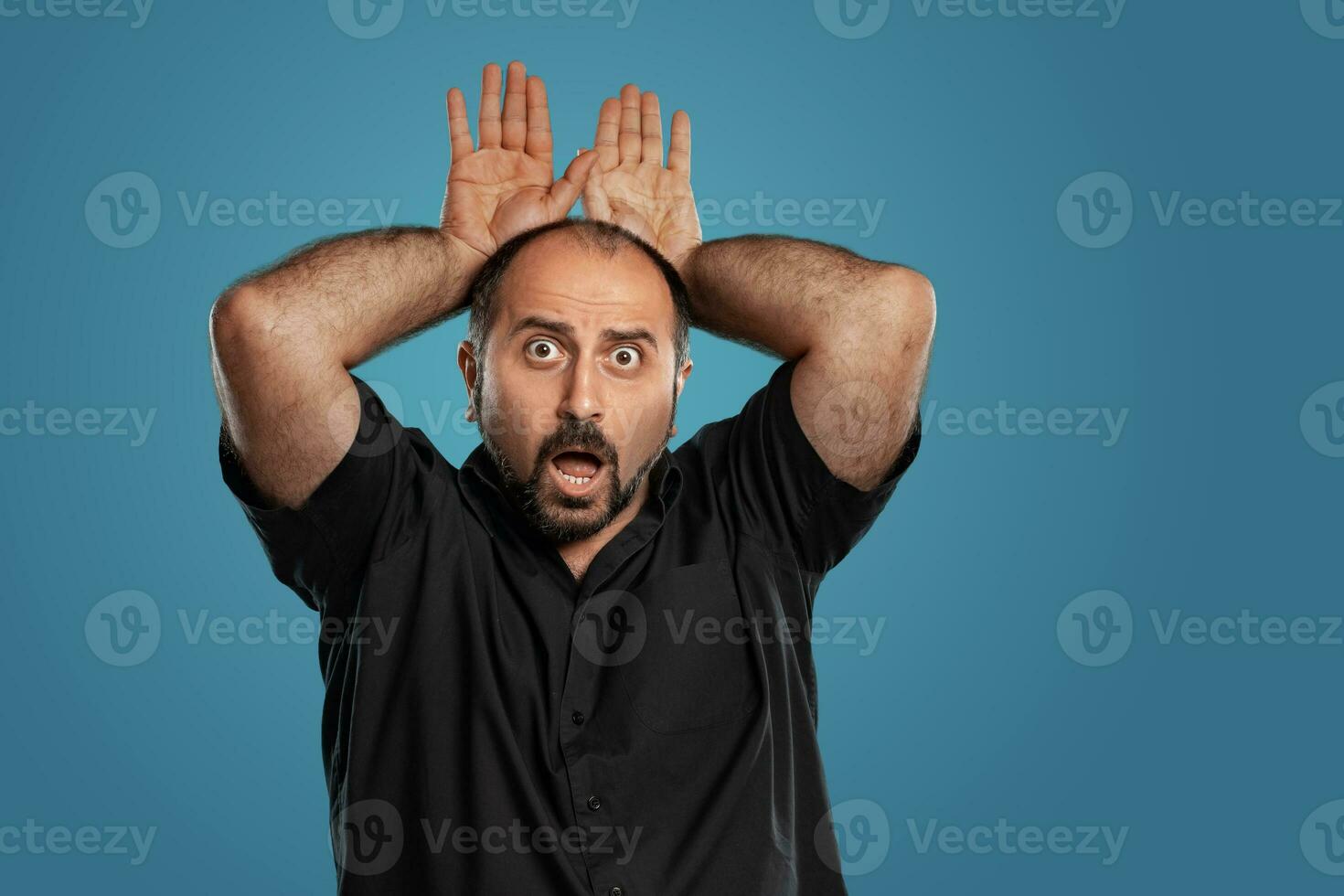 Close-up portrait of a brunet middle-aged man with beard, dressed in a black t-shirt and posing against a blue background. photo