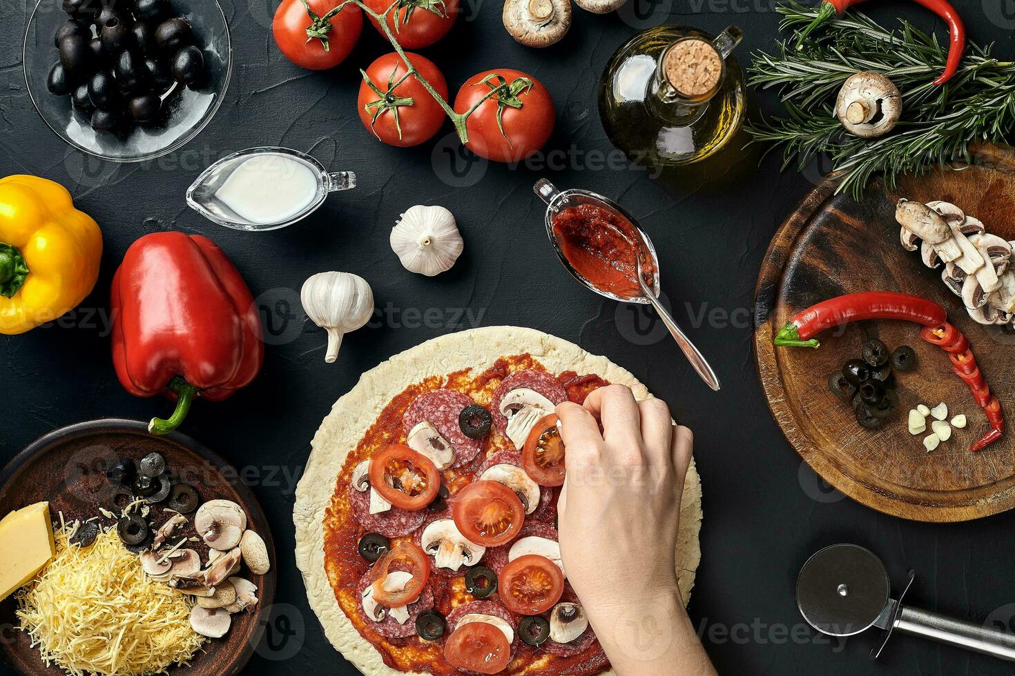 Hands of baker adding ingredients into pizza during pizza preparation at kitchen photo