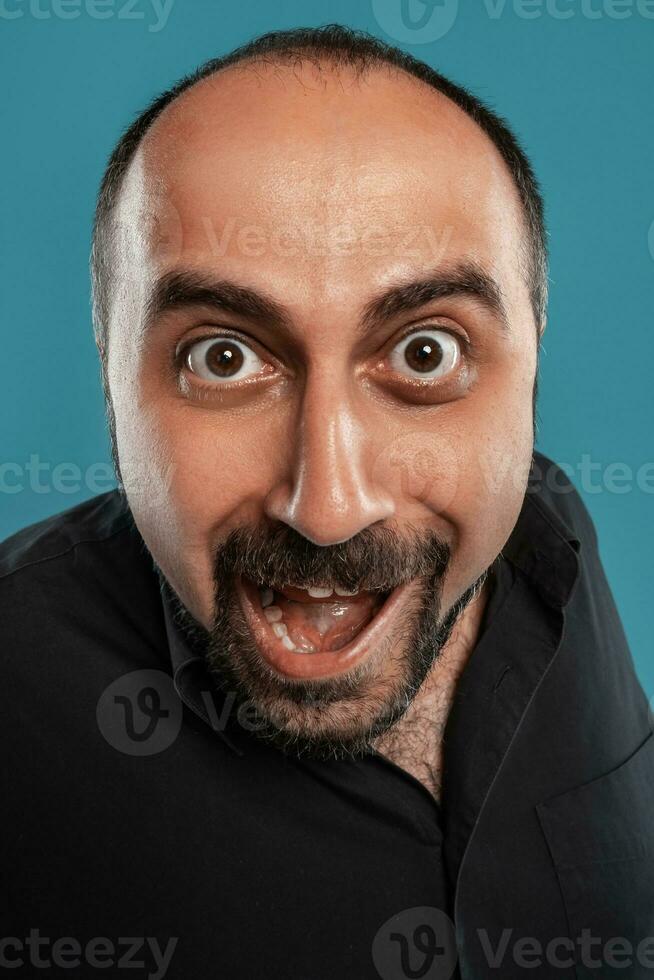 de cerca retrato de un moreno de edad mediana hombre con barba, vestido en un negro camiseta y posando en contra un azul antecedentes. foto