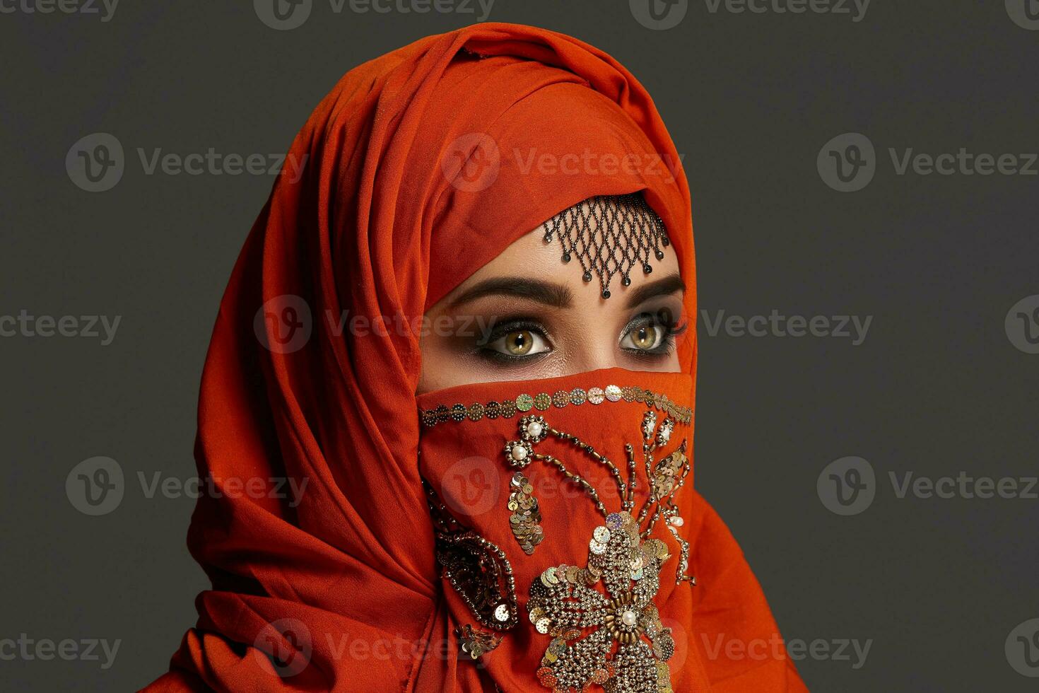 Studio shot of a young charming woman wearing the terracotta hijab decorated with sequins and jewelry. Arabic style. photo