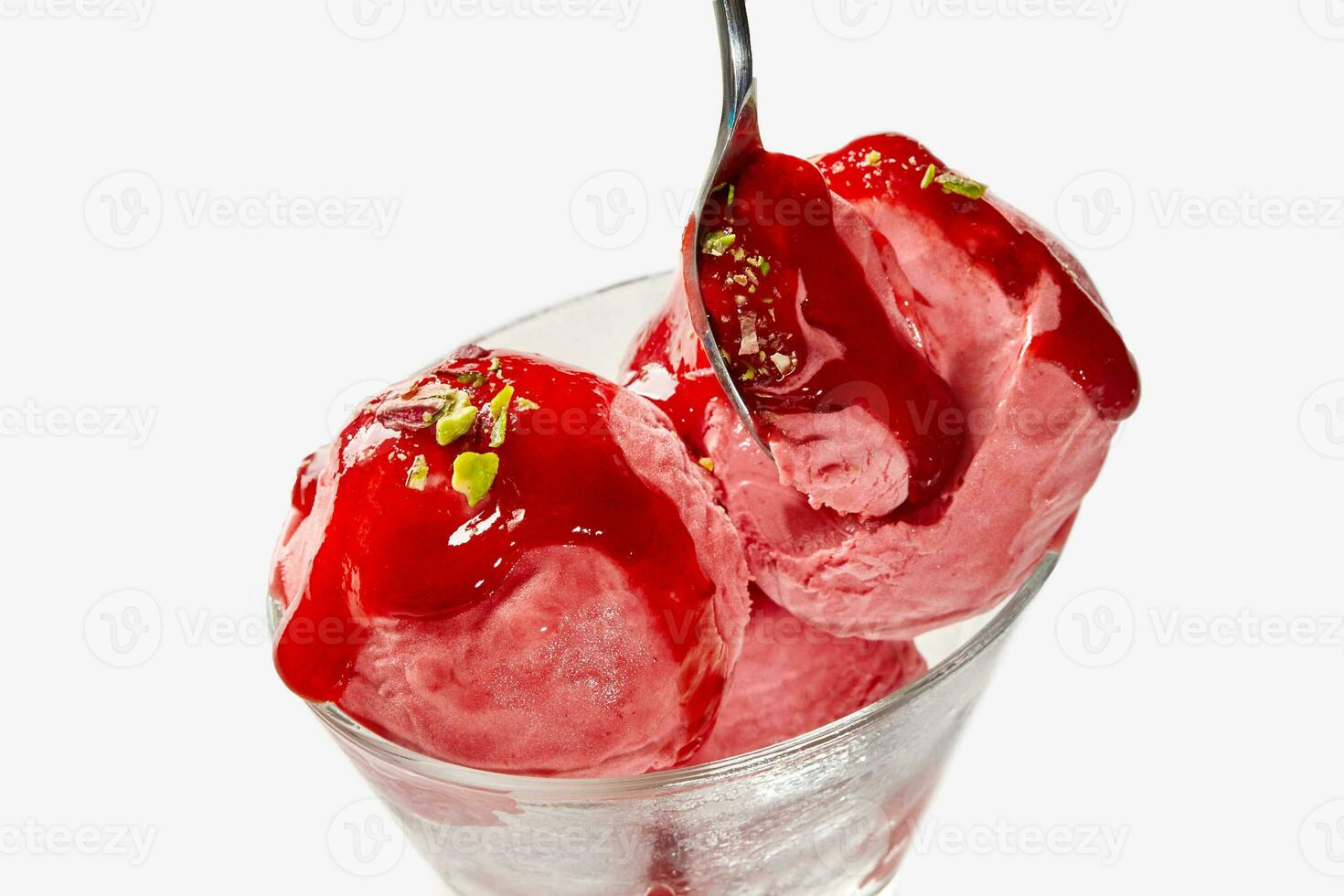 Scoops of fruit ice cream topped with berry jam and pistachio crumbs in glass bowl with spoon photo