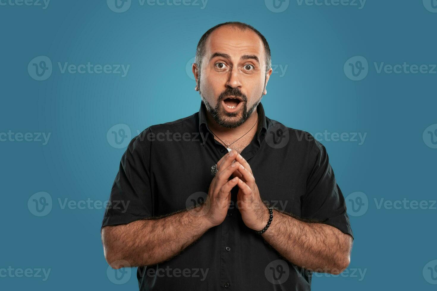 Close-up portrait of a brunet middle-aged man with beard, dressed in a black t-shirt and posing against a blue background. photo