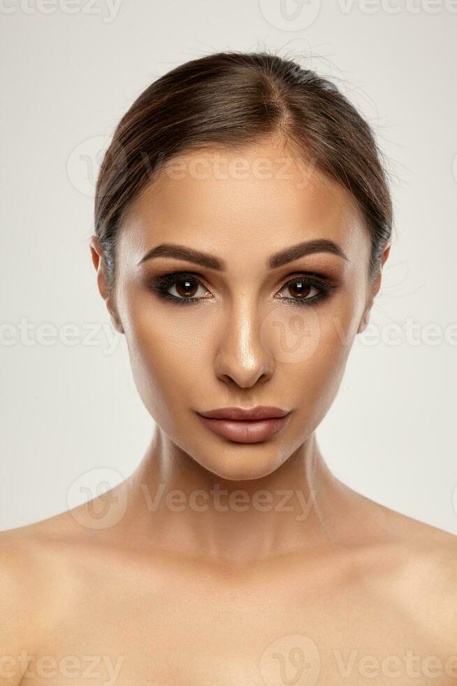 Close up portrait of a brunette nude model girl with professional evening make-up and plump lips, posing on gray background. photo