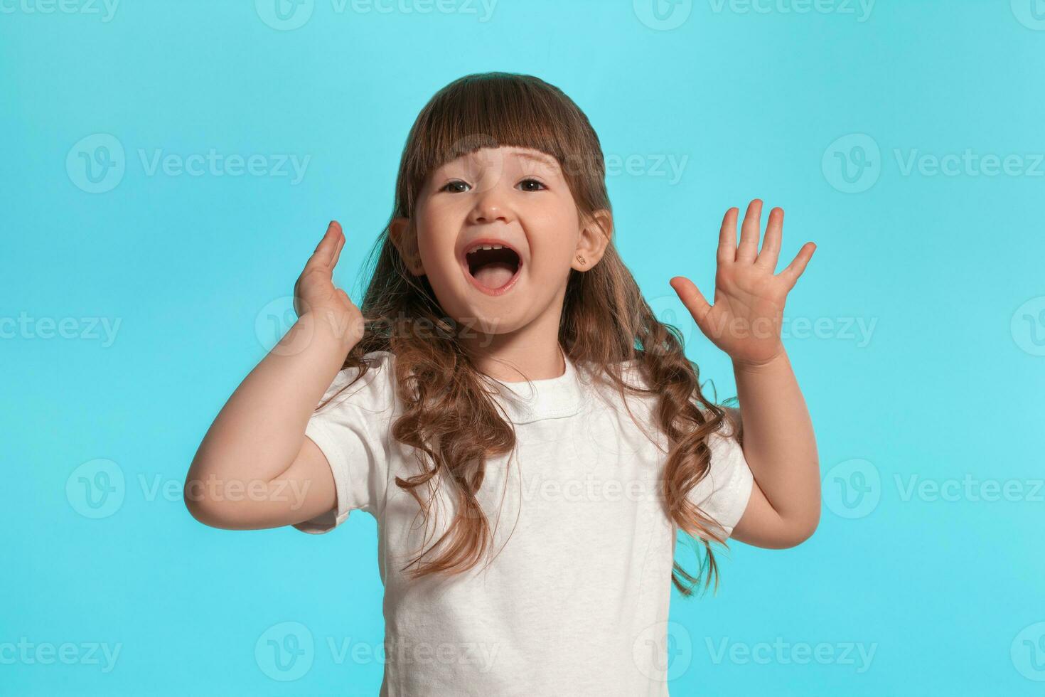 Beautiful little girl wearing in a white t-shirt is posing against a blue studio background. photo