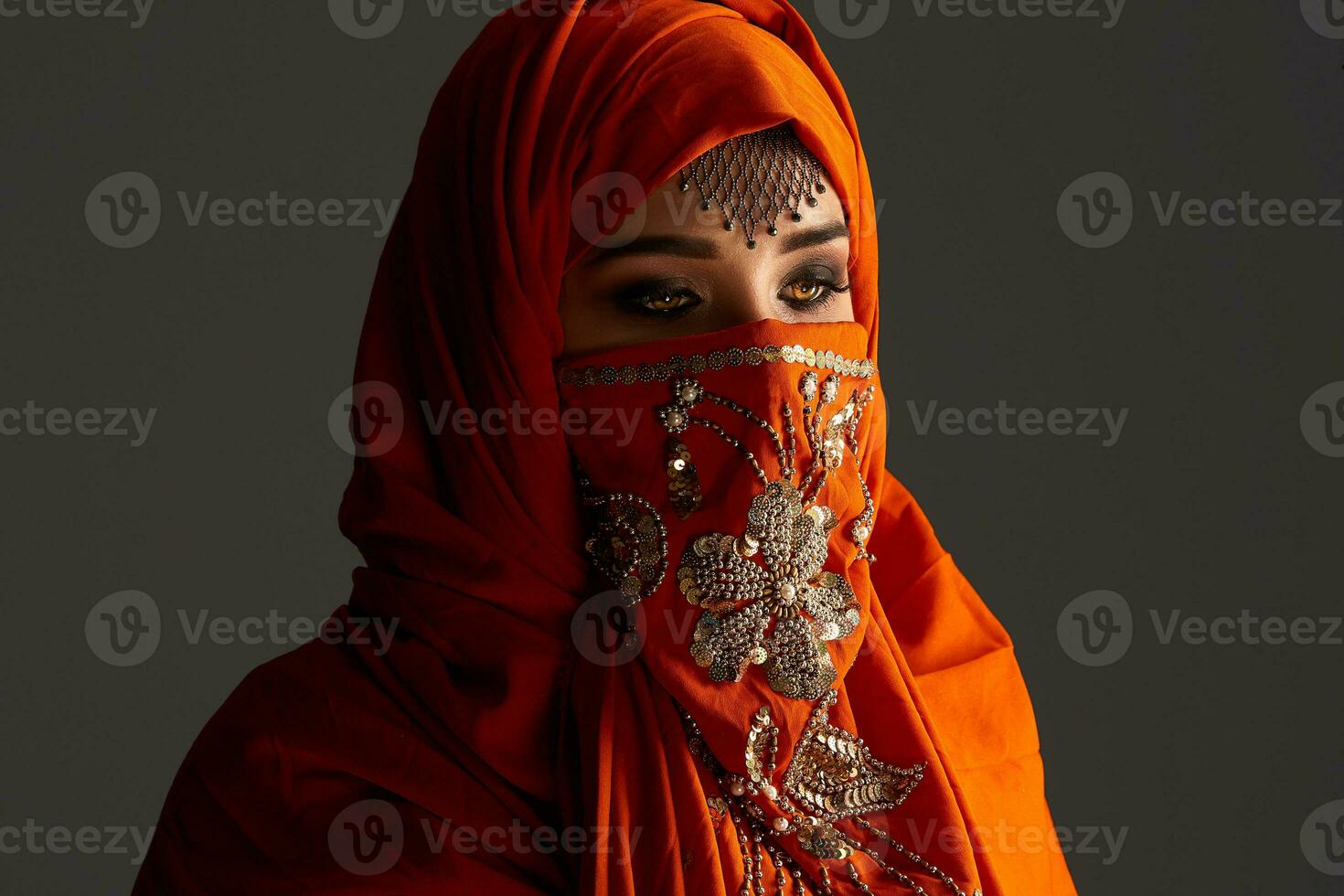Studio shot of a young charming woman wearing the terracotta hijab decorated with sequins and jewelry. Arabic style. photo