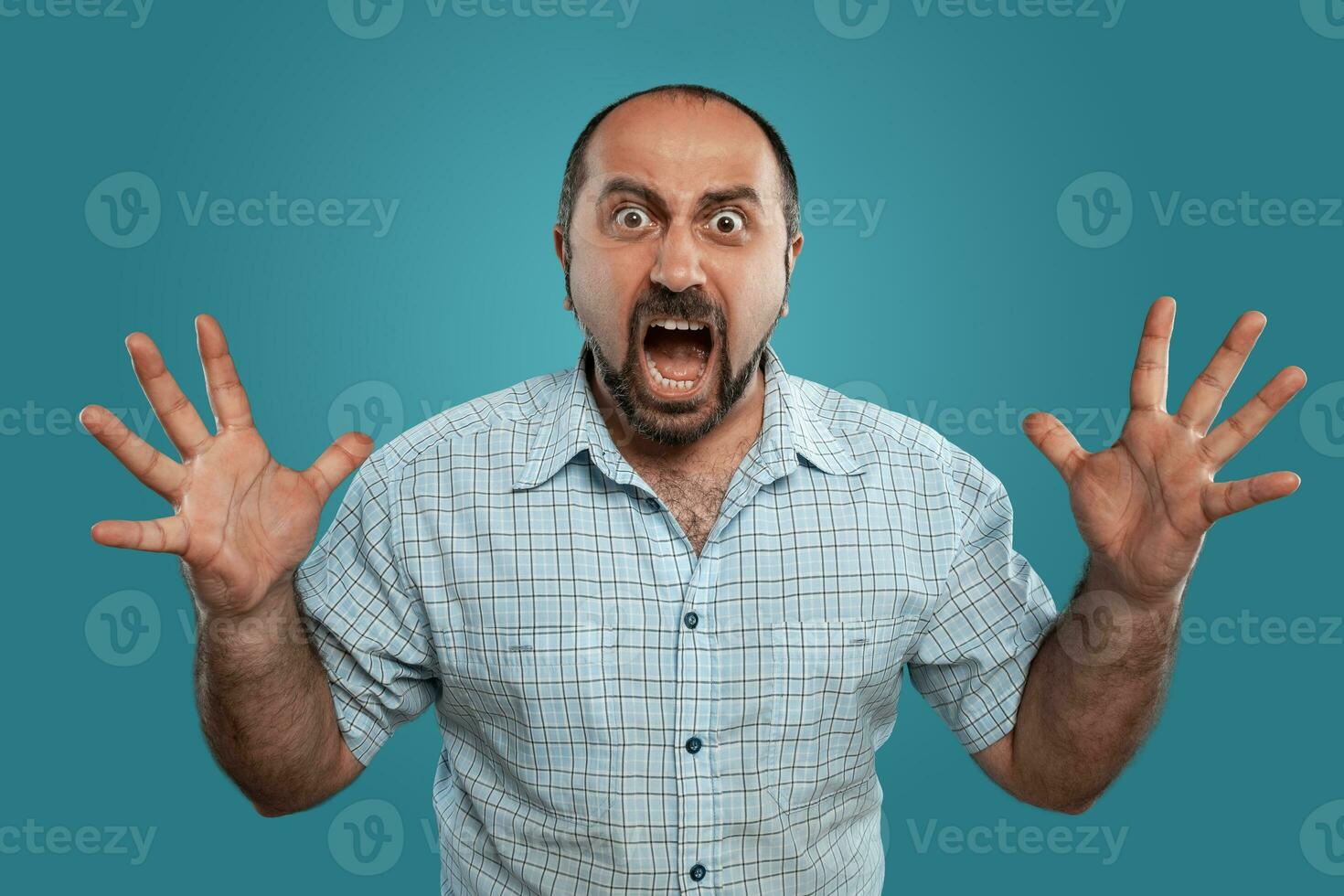 Close-up portrait of a brunet middle-aged man with beard, dressed in a light checkered shirt and posing against a blue background. photo